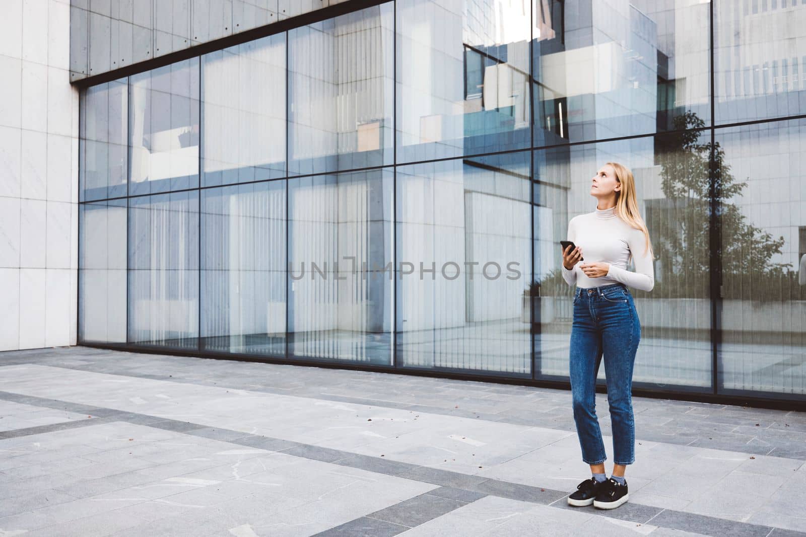 Young caucasian woman in an urban modern setting, office buildings in the background, using a mobile device. Business woman on a break.