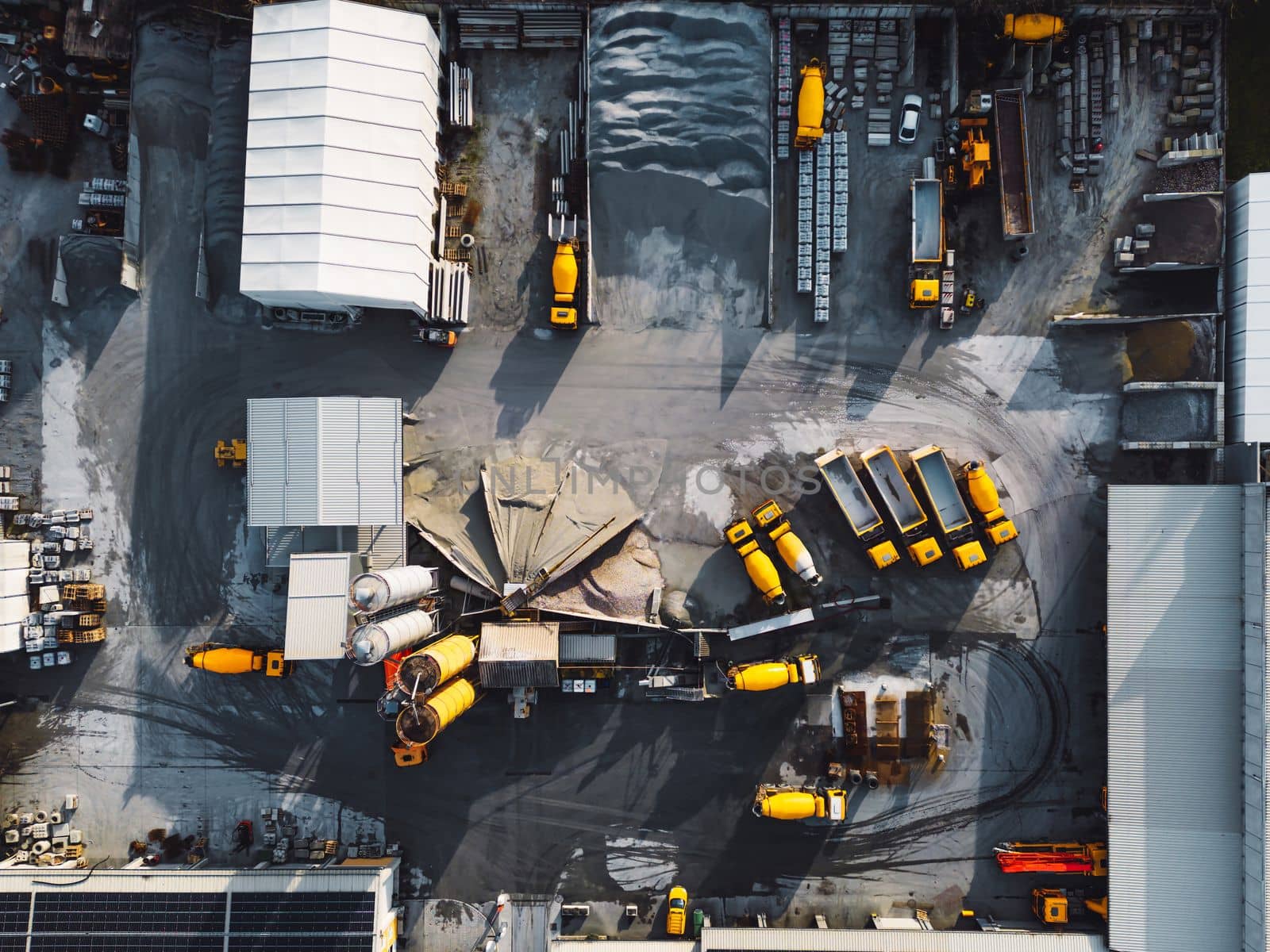 Aerial view in industrial area, directly above concrete factory, firm with lots of heavy machinery on the grounds, yellow trucks and other vehicles.