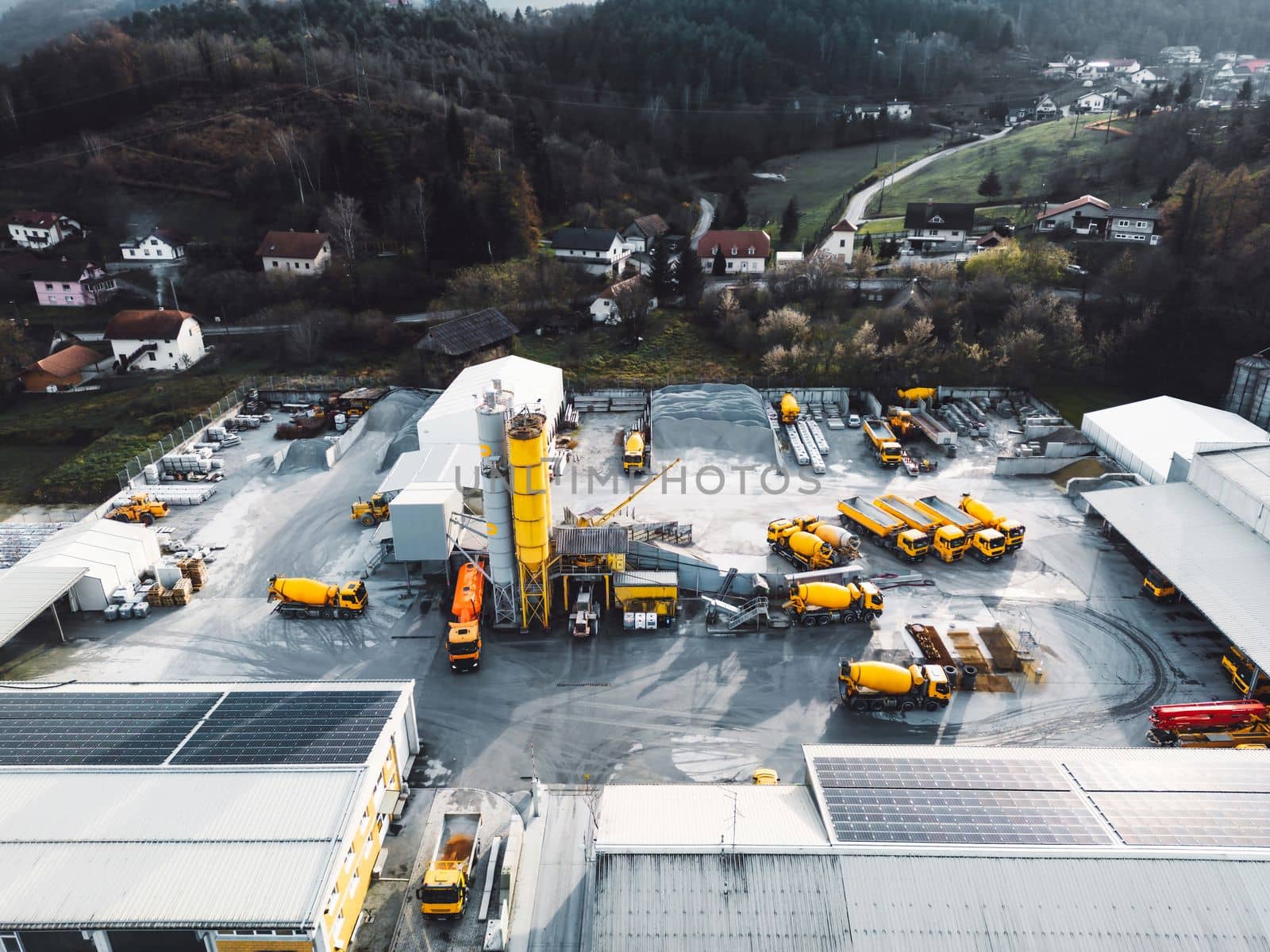 Aerial view in industrial area, directly above construction company, firm with lots of heavy machinery on the grounds, yellow trucks and other vehicles.