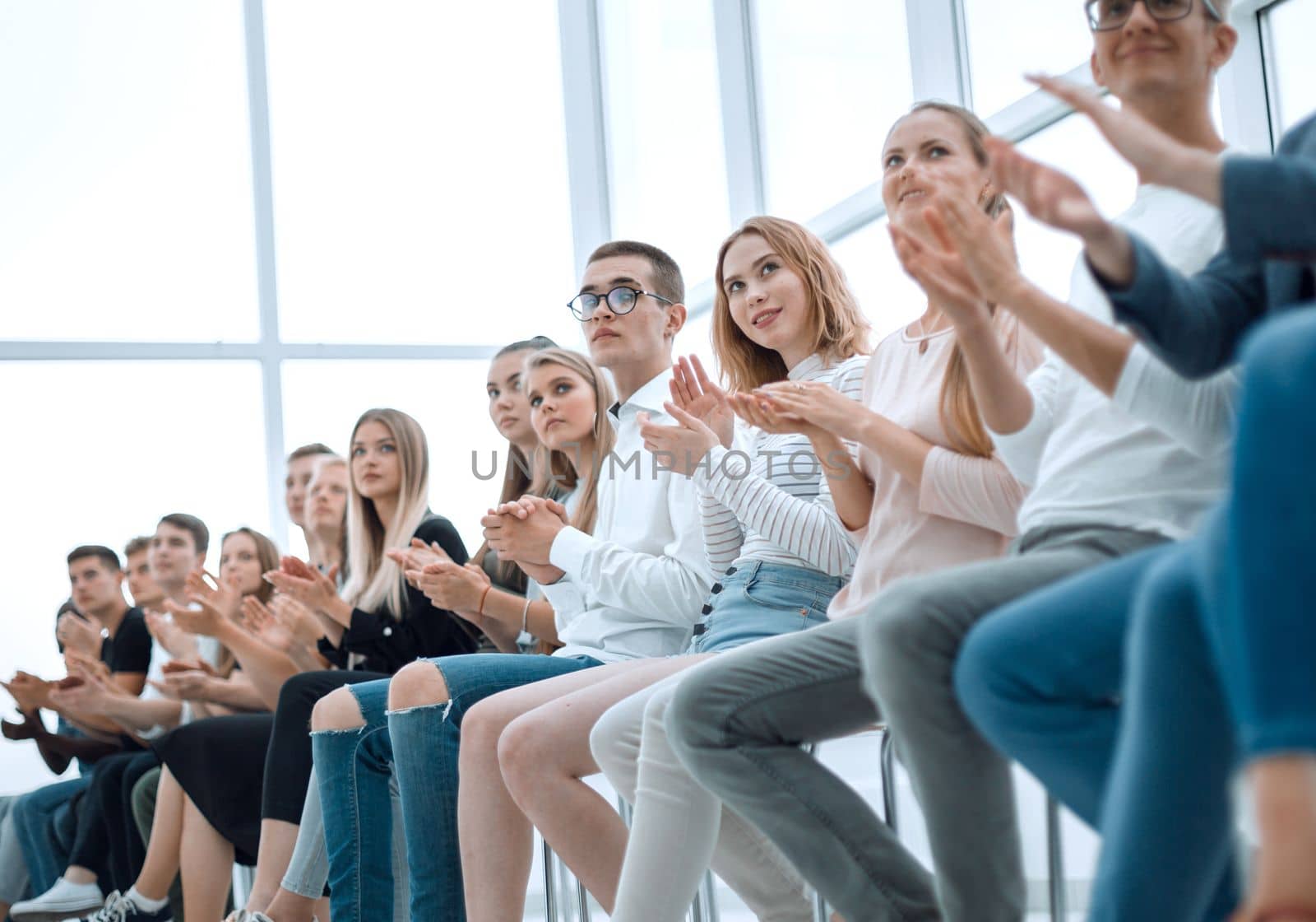 large group of diverse young people sitting in a row and applauding. photo with copy space
