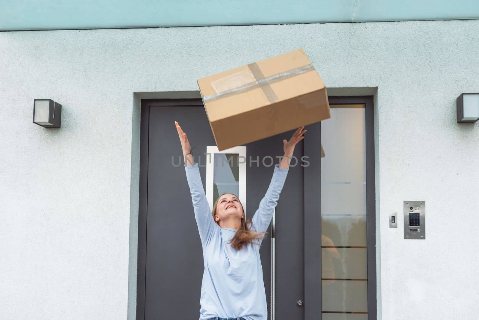 Waist up caucasian woman throwing an exciting package in the air, standing outside her front door by VisualProductions