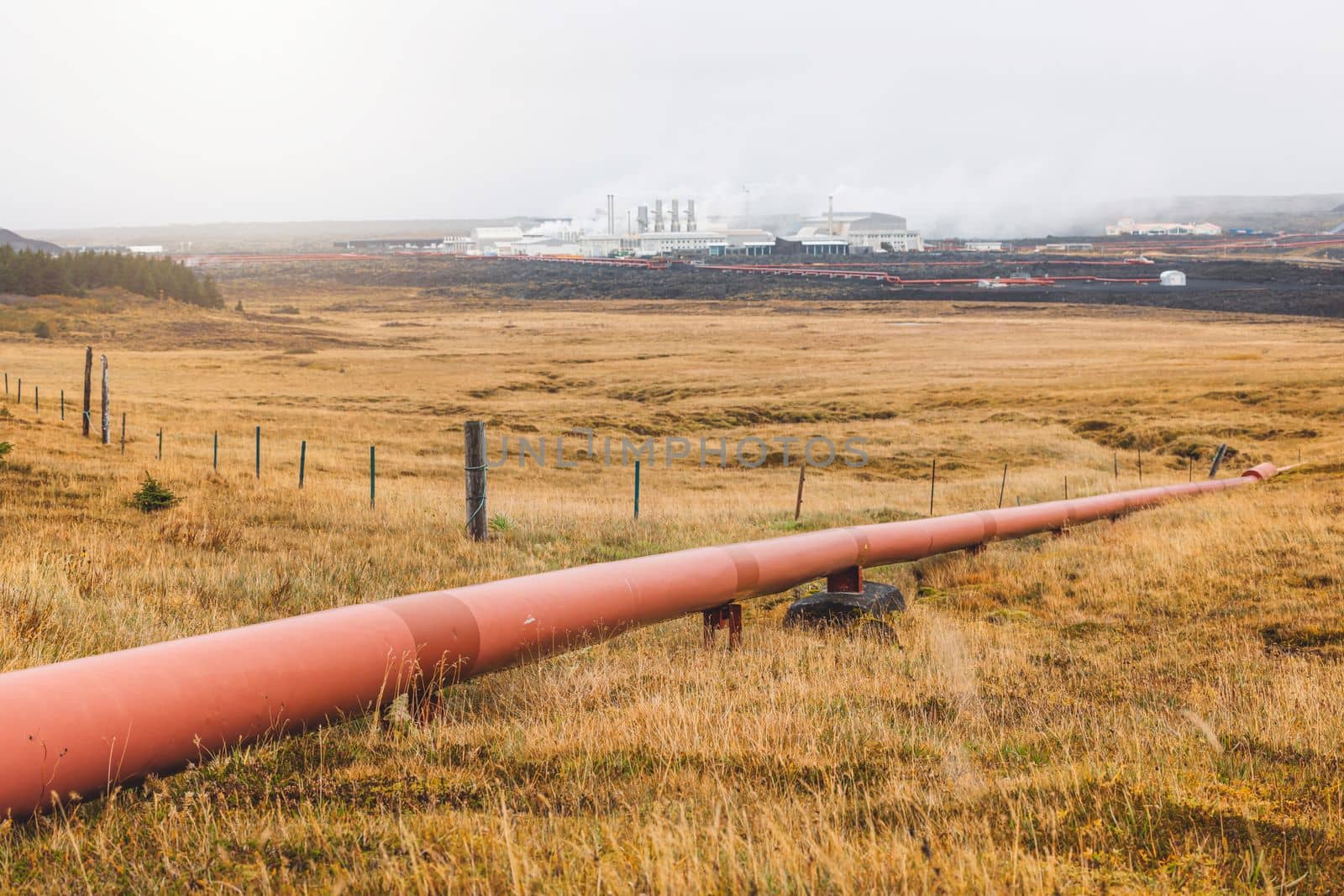 Geothermal Power Plant, hot water power station in Iceland. Steam rolling out of the plant chimneys, red large tubes running across the grounds filled with hot water. Sustainable, energy efficient Cloudy cold autumn day in Iceland.