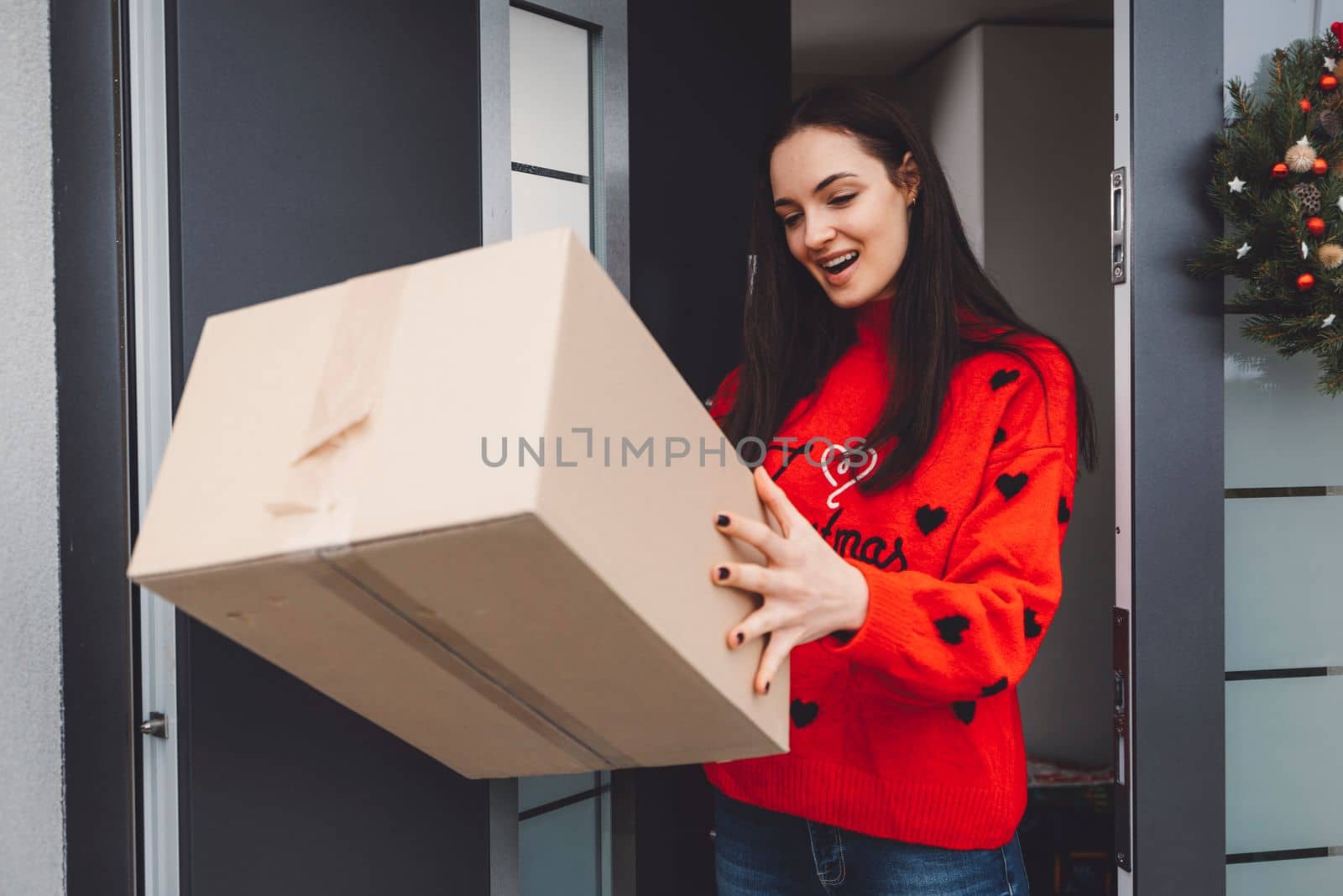 Cheerful young woman excited over a package she just received. Woman getting her christmas gift in the mail. Opening the Christmas present at home.