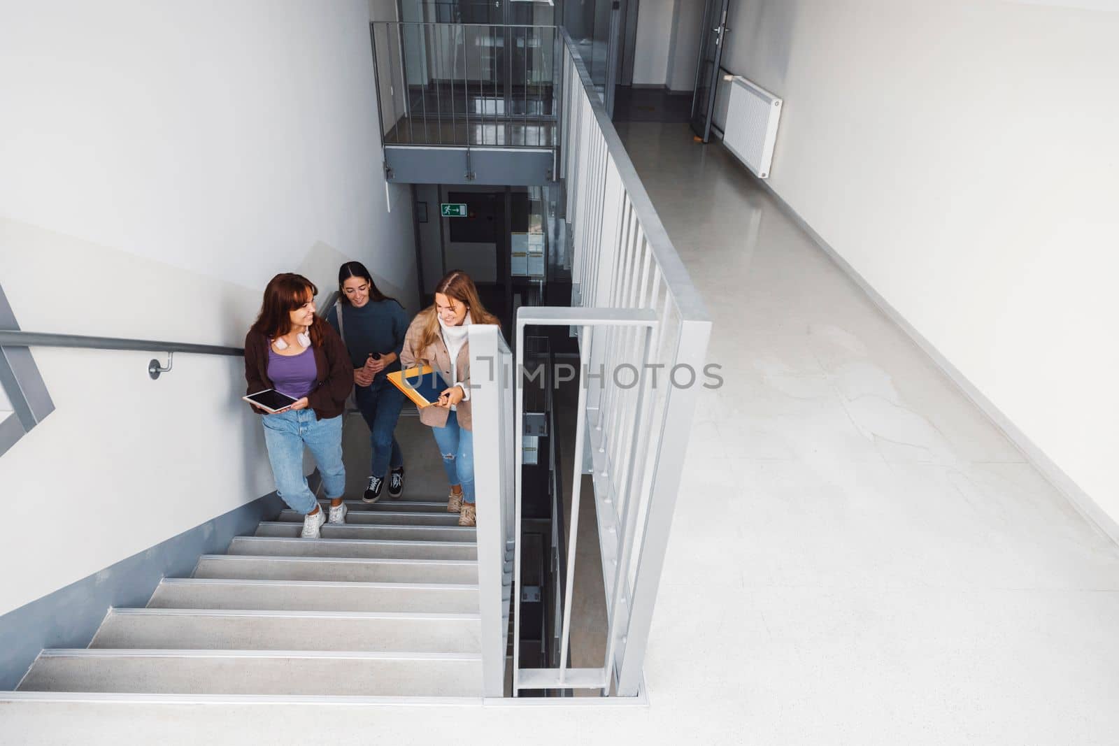 Group of three friends, young caucasian women students walking inside the school during a break, headed to another classroom. Students carrying their books with them.