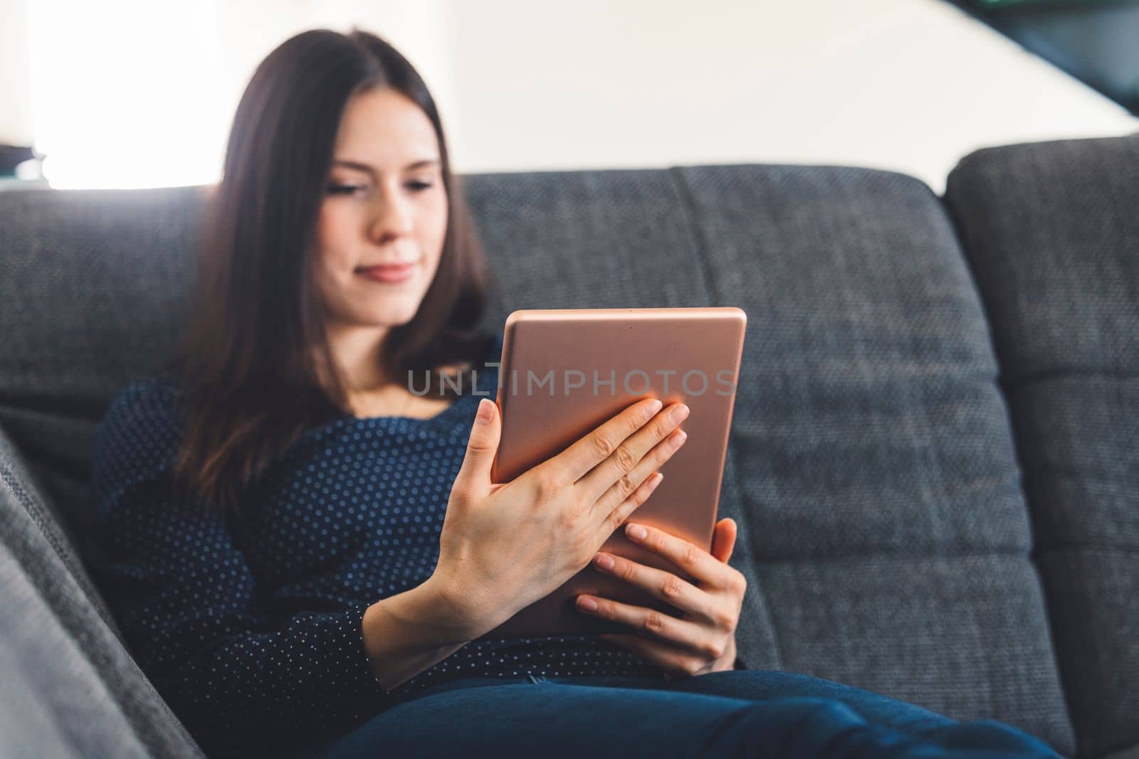 Young woman with brown hair sitting on the sofa online shopping on the digital tablet by VisualProductions