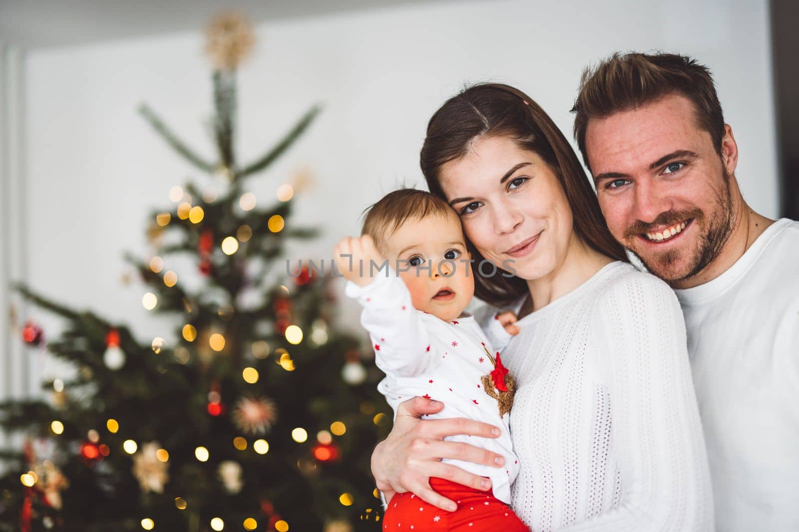 Happy young cheerful caucasian family of three mom dad and baby girl having fun decorating the Christmas tree. Family Christmas portrait.