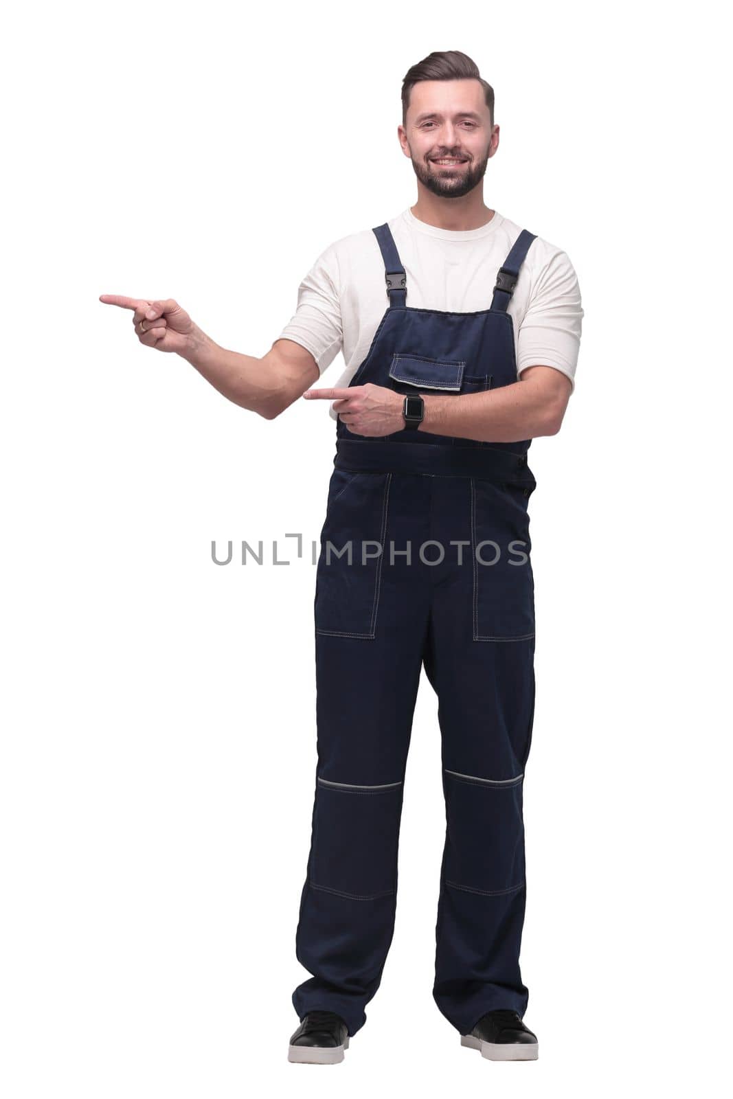 in full growth. smiling man in overalls pointing to a copy of the space . isolated on white