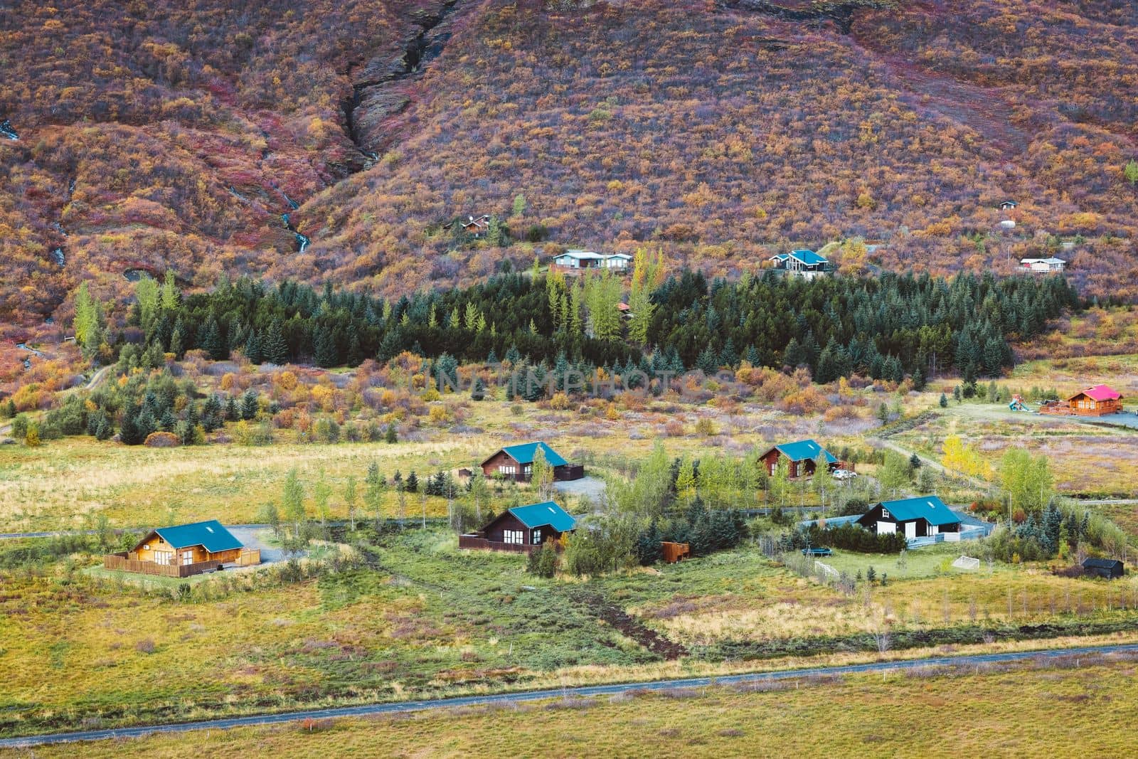 Little cottages in Iceland. Autumn nature, forest covered hill in the background.