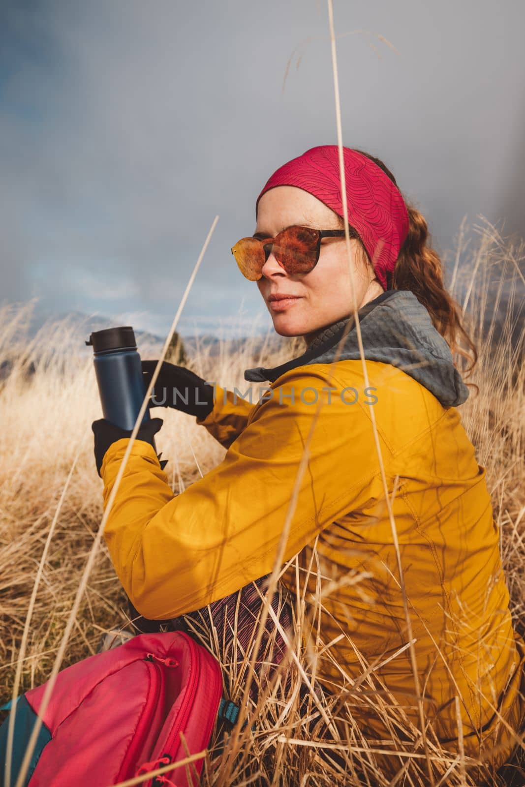 Waist up woman hiker looking away from the camera holding a blue thermo flask in her hands, hiking on a foggy autumn day,