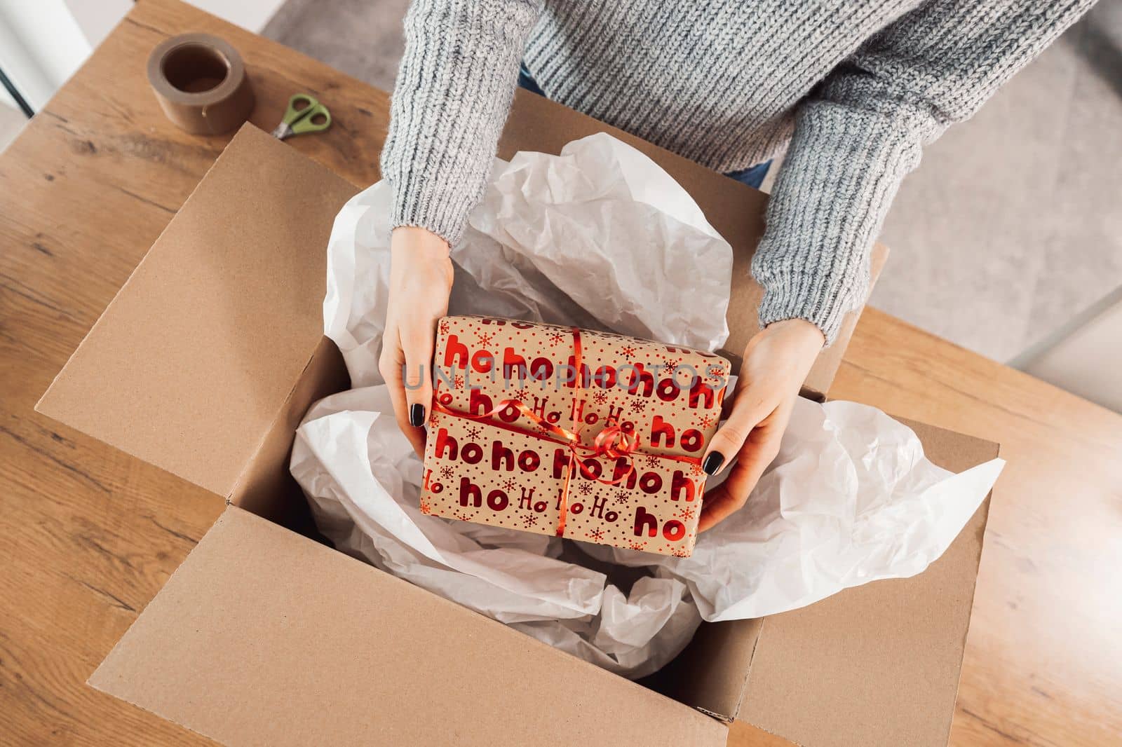Top down view woman hands holding a Christmas present, putting it inside a cardboard box, ready to send in the mail by VisualProductions