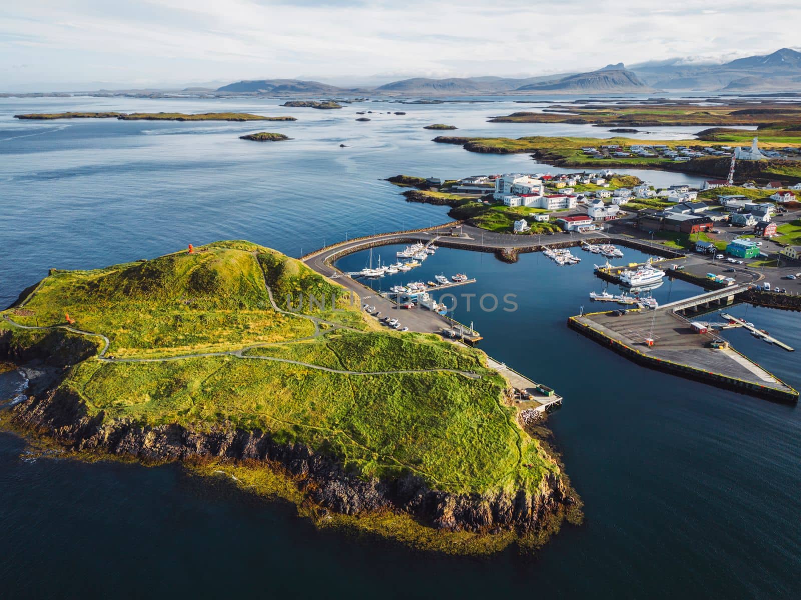 Beautiful aerial view of the Stykkisholmskirkja Harbor with Fishing ships boats at Stykkisholmur town in western Iceland. City view from Sugandisey Cliff with lighthouse. Famous colorful houses. September, autumn 2022.