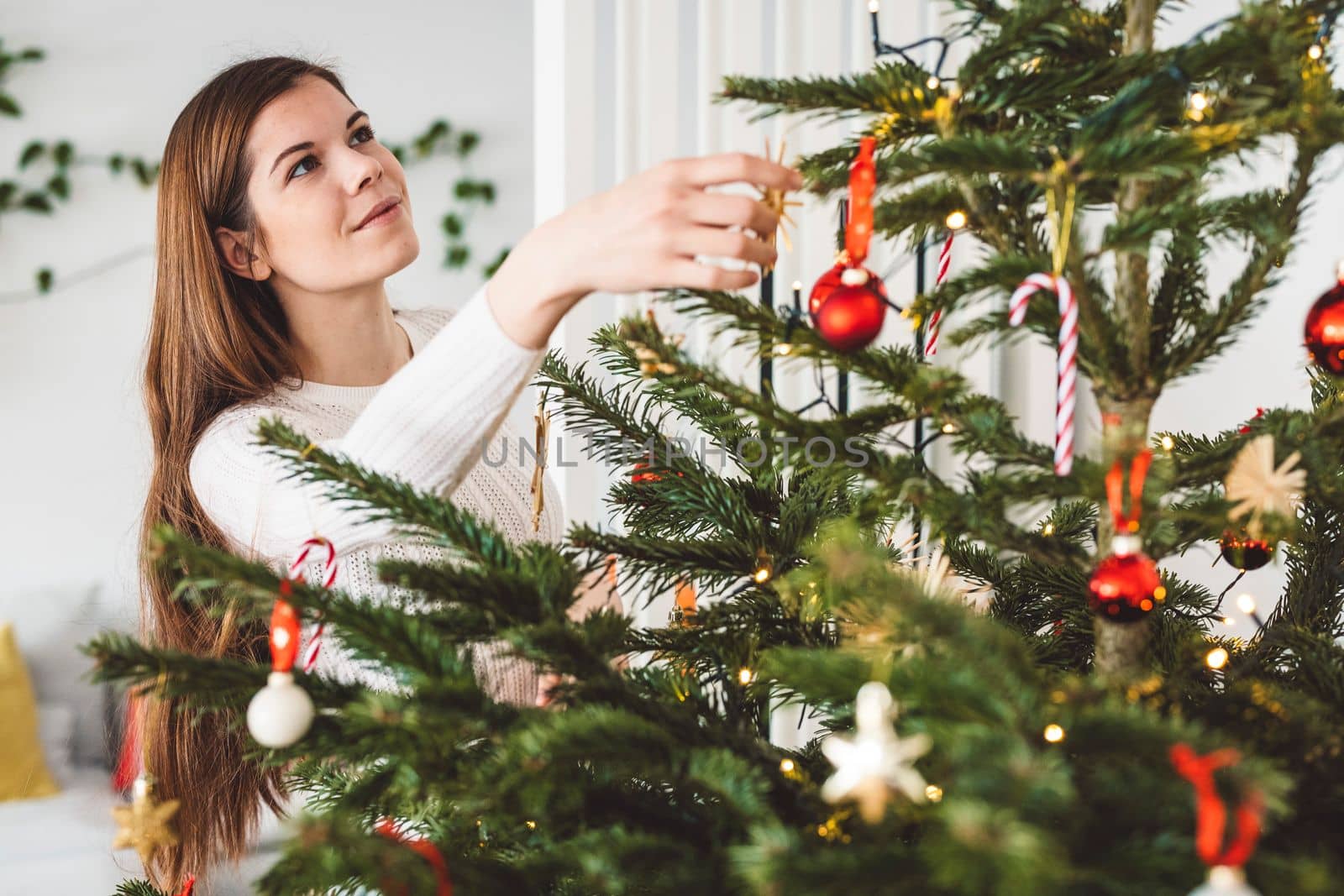 Smiling caucasian woman looking up at the natural Christmas tree she is decorating by herself by VisualProductions