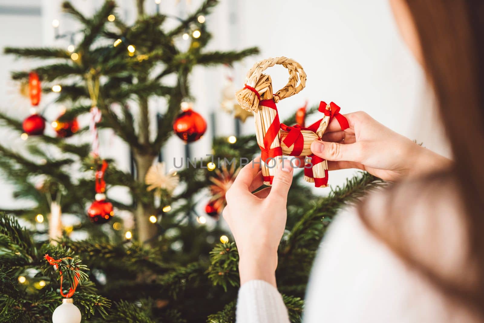 Unrecognizable caucasian woman decorating the Christmas tree, putting red ornament on the tree, holding a red Christmas ornament.