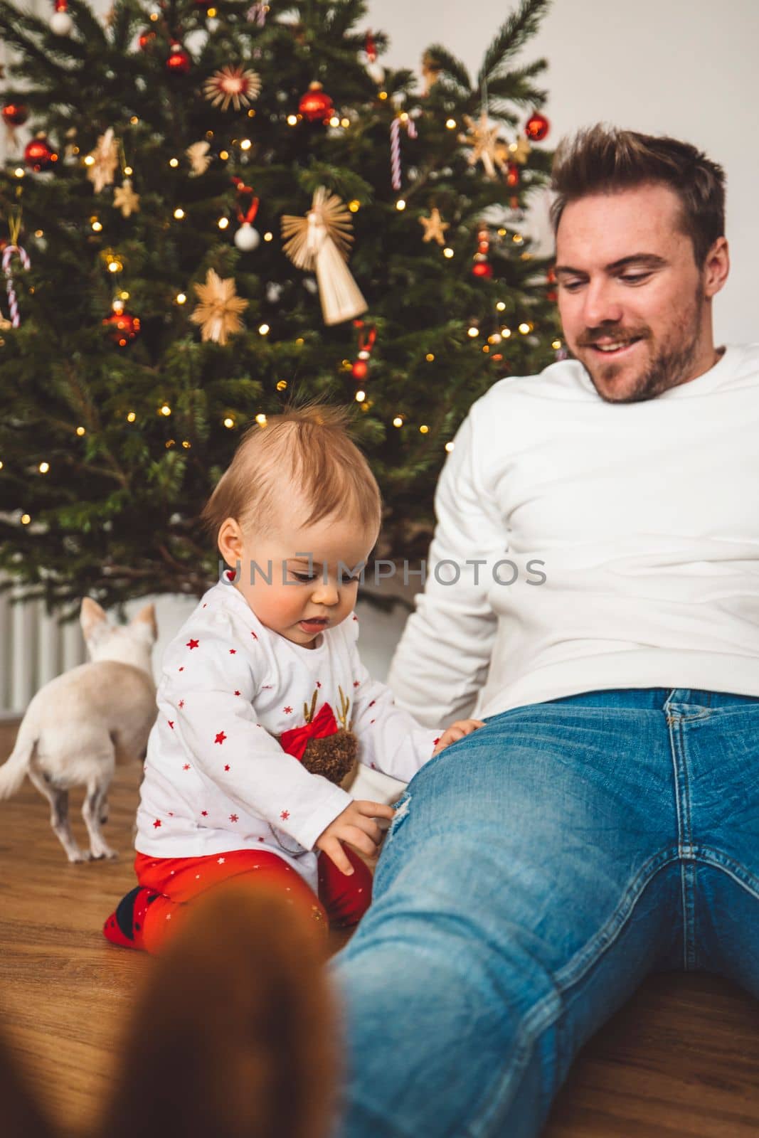 Cute baby girl with her dad sitting next to the Christmas tree by VisualProductions