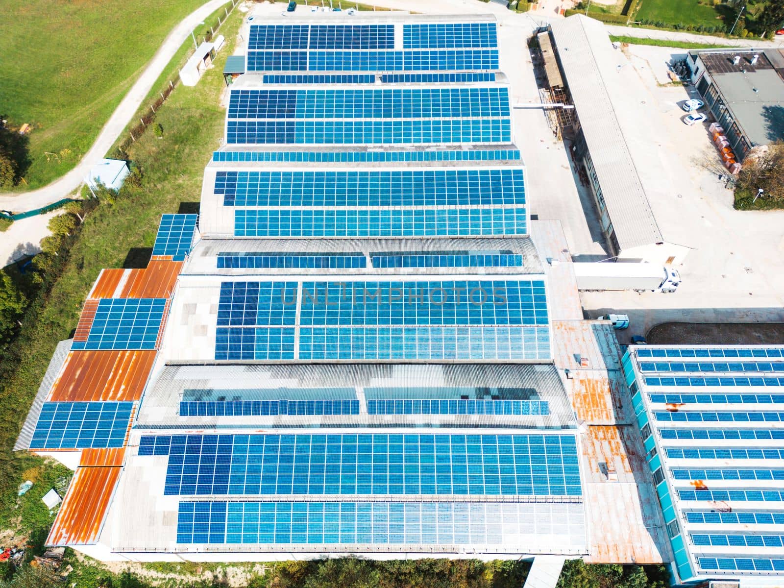 Solar panels installed on a roof of a large industrial building or a warehouse. Industrial building in the country side of Slovenia with residential houses in the background. High quality photo