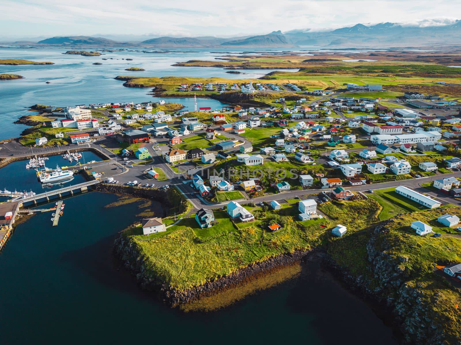 Beautiful aerial view of the Stykkisholmskirkja Harbor with Fishing ships boats at Stykkisholmur town in western Iceland. City view from Sugandisey Cliff with lighthouse. Famous colorful houses. September, autumn 2022.