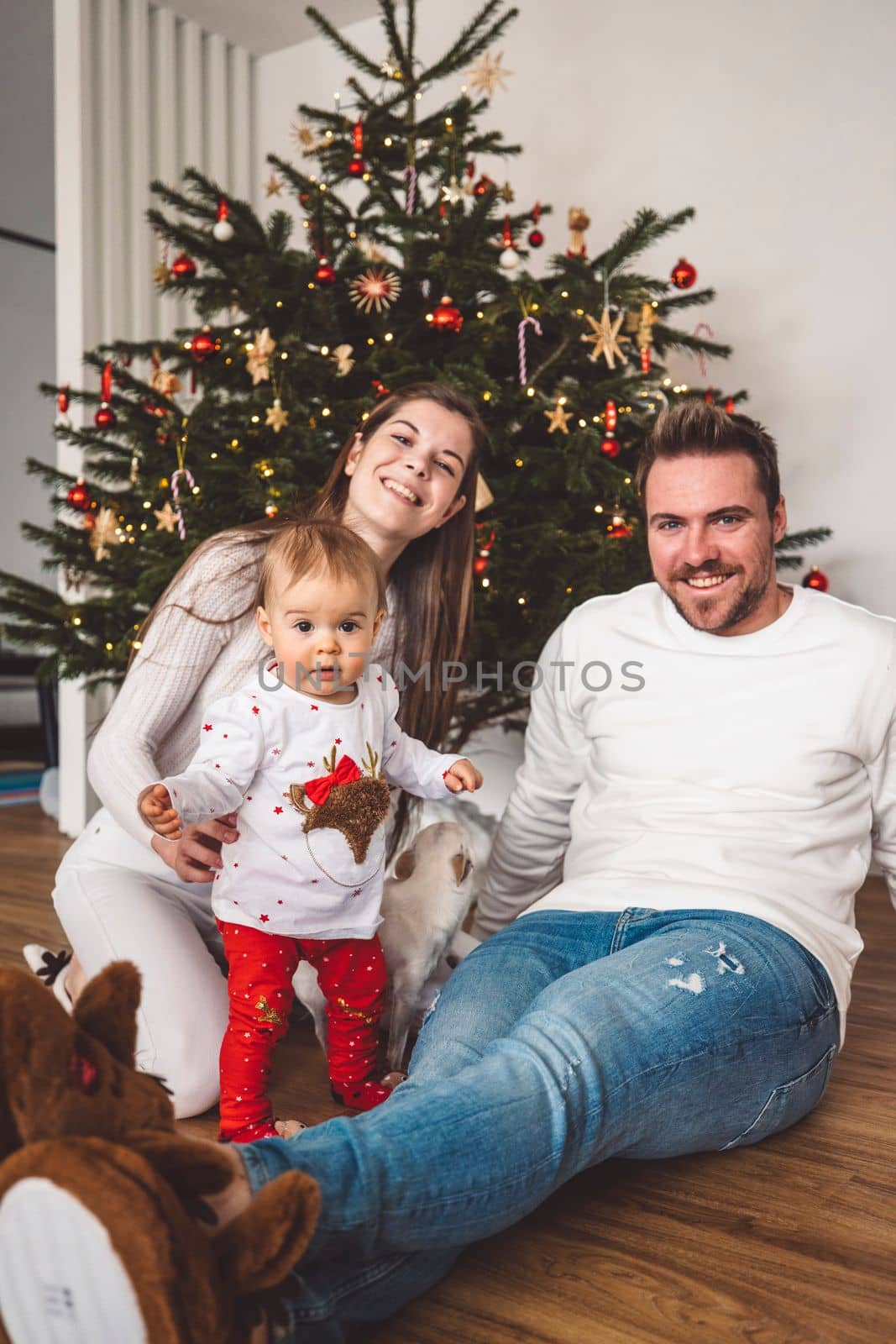 Happy young cheerful caucasian family of three mom dad and baby girl having fun decorating the Christmas tree. Family Christmas portrait. 