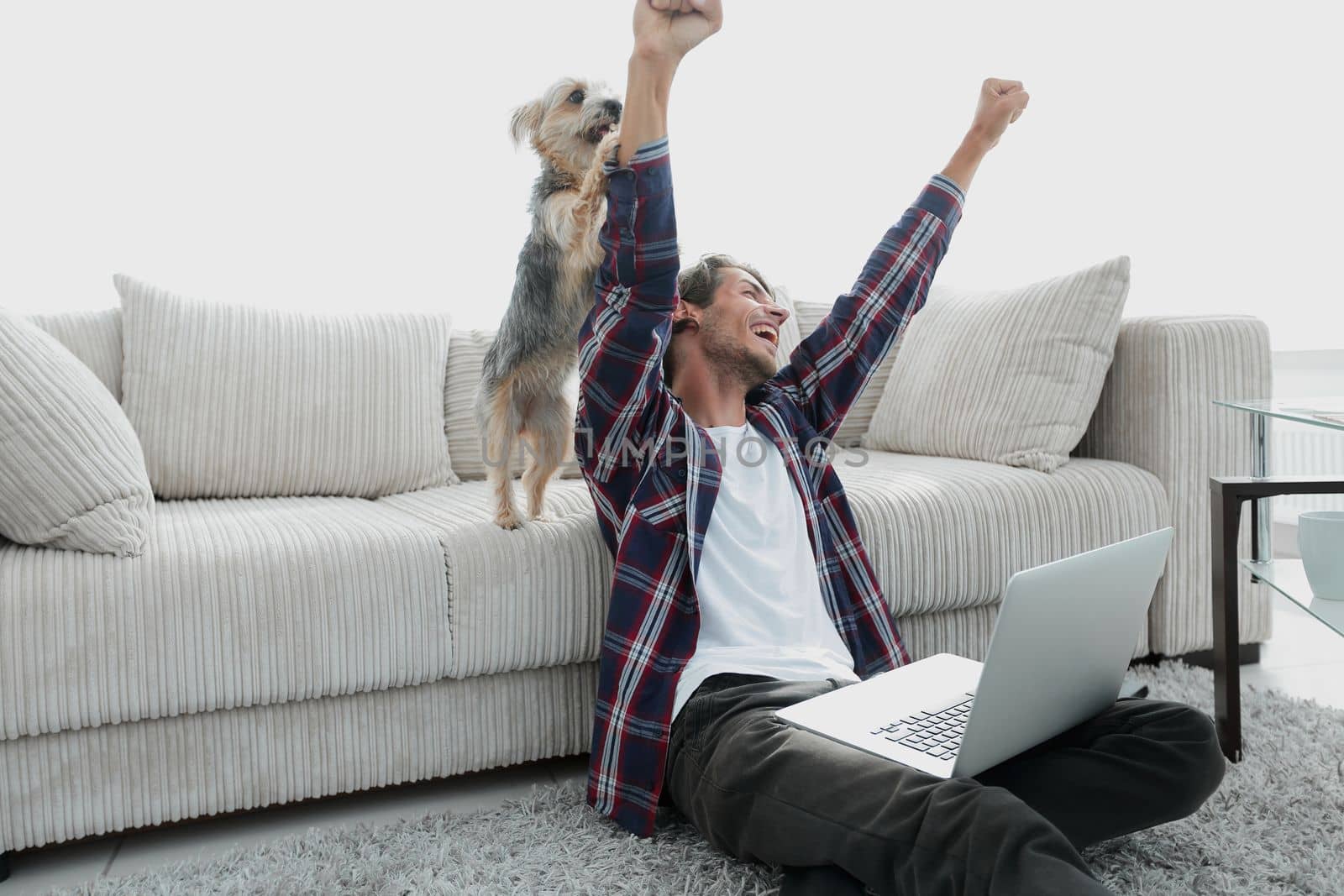 happy guy exults with his dog sitting near the sofa in the living room. by asdf