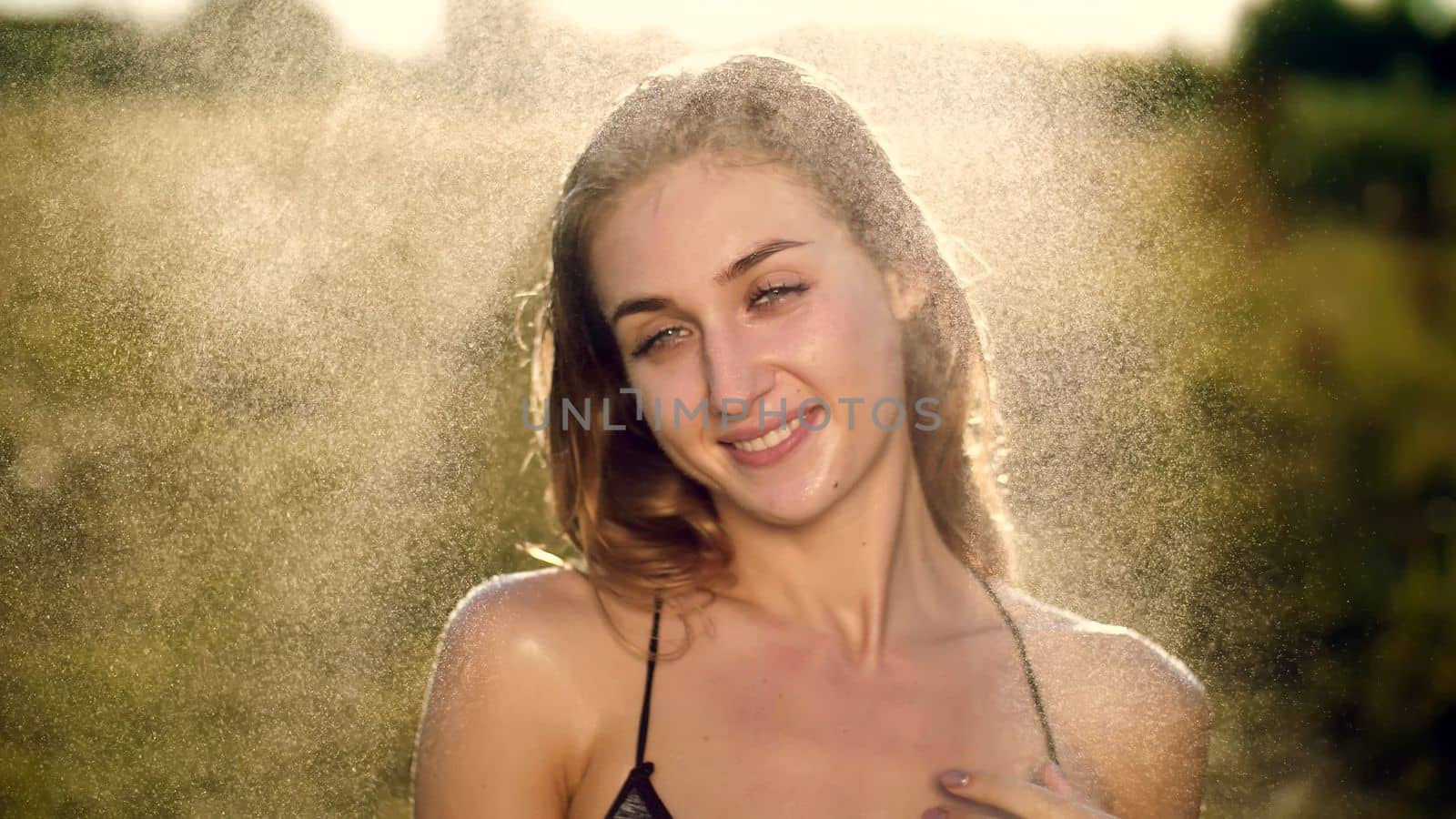 Portrait of a sexy, beautiful young blonde girl, under a light summer rain, in the sun rays, on a green meadow. The girl smiles, Her skin shines, radiates health. Image of happiness. High quality photo