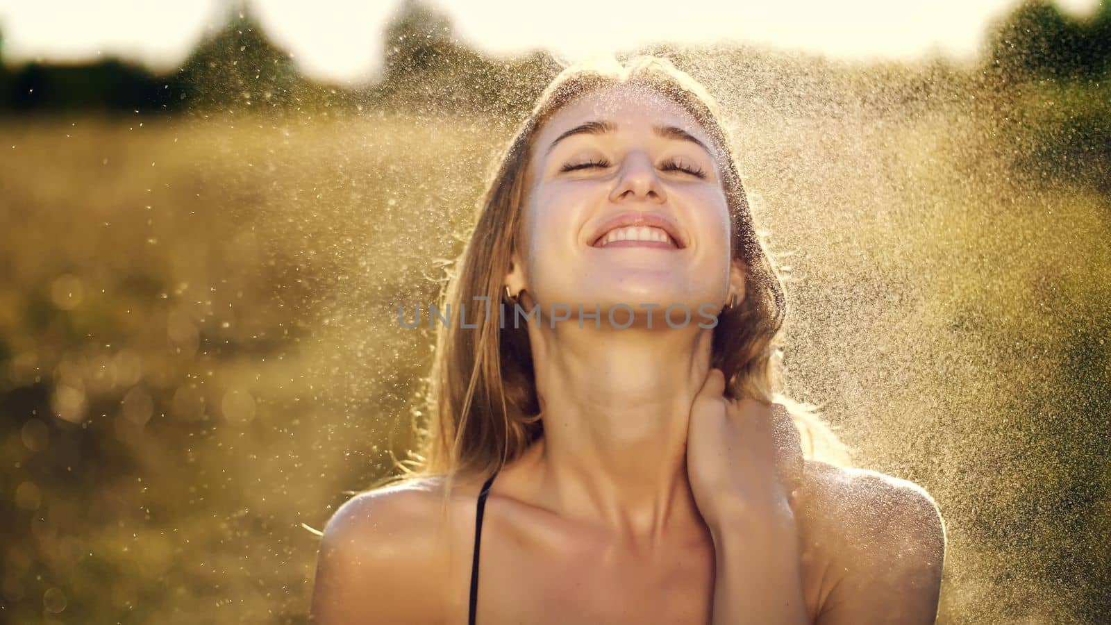 Portrait of a beautiful young blonde girl, under light summer rain, in the sun rays, on a green meadow. The girl smiles, strokes herself over the delicate, beautiful white skin. High quality photo