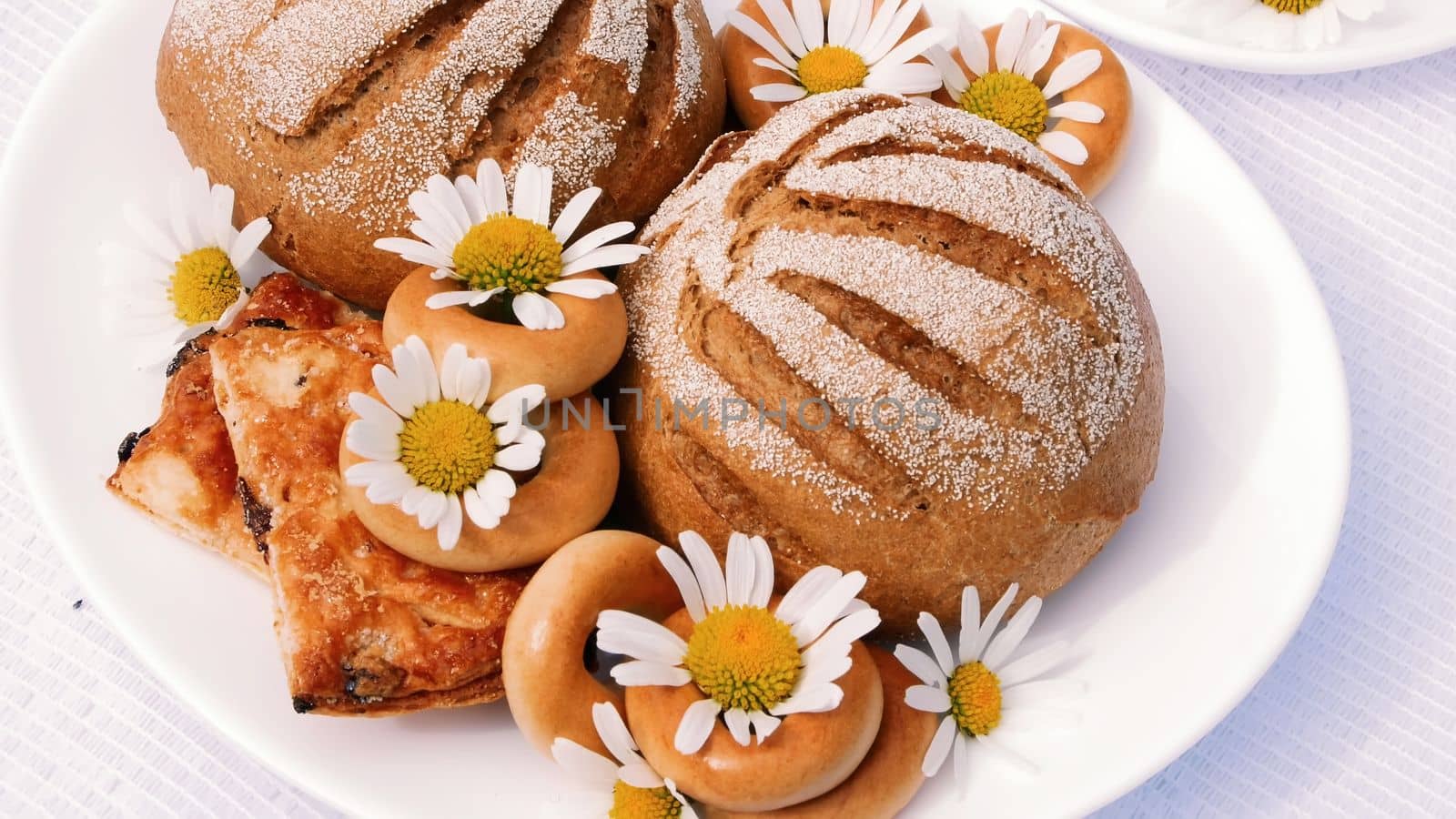 A close-up, a white plate with pastries, biscuits and cookies, decorated with white daisies. On white saucers there are two white cups with chamomile tea. High quality photo