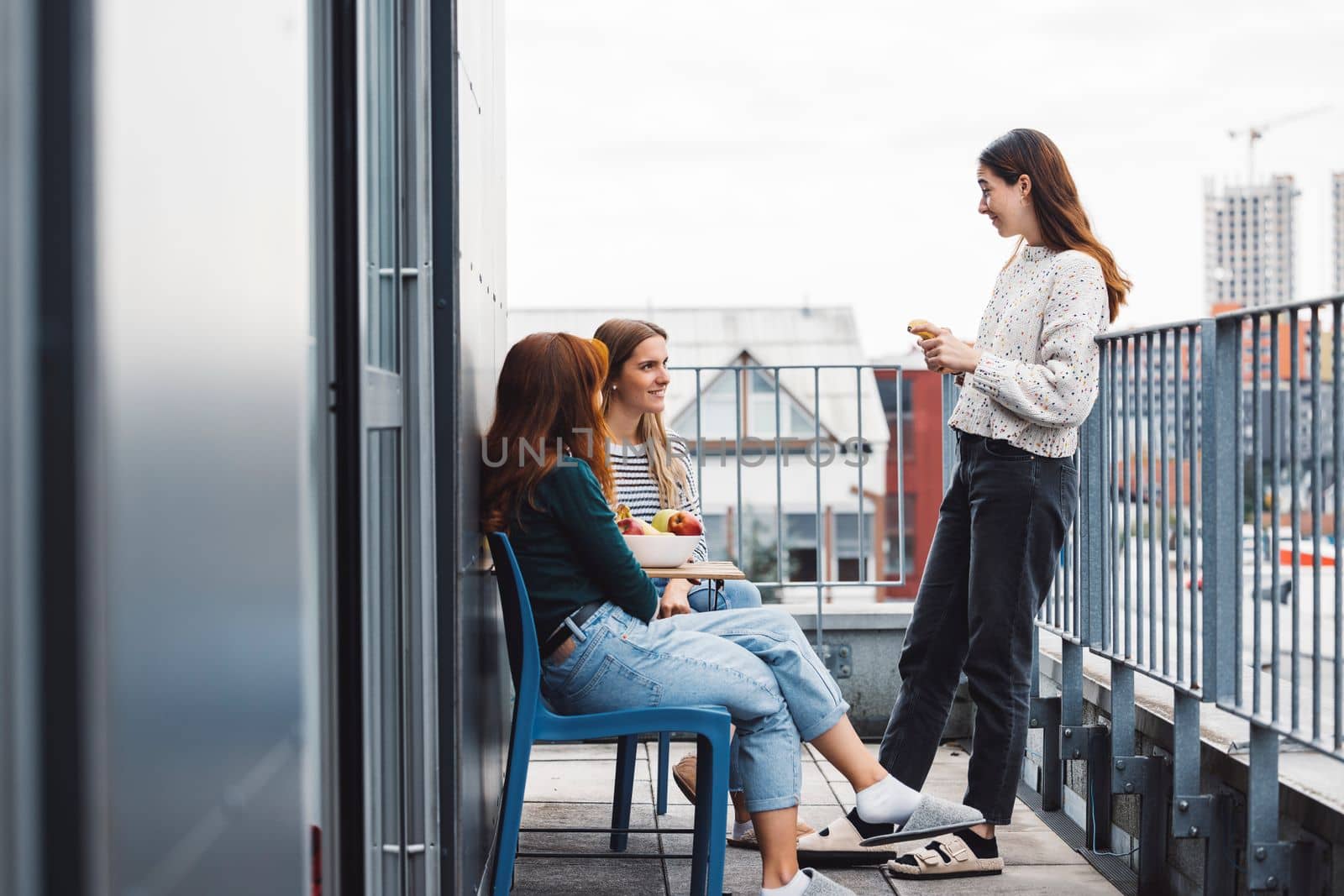 Young caucasian woman college students, sitting on the rood top of their dorm room, eating a snack taking a break from studying, getting some fresh air, on a cloudy autumn day. 
