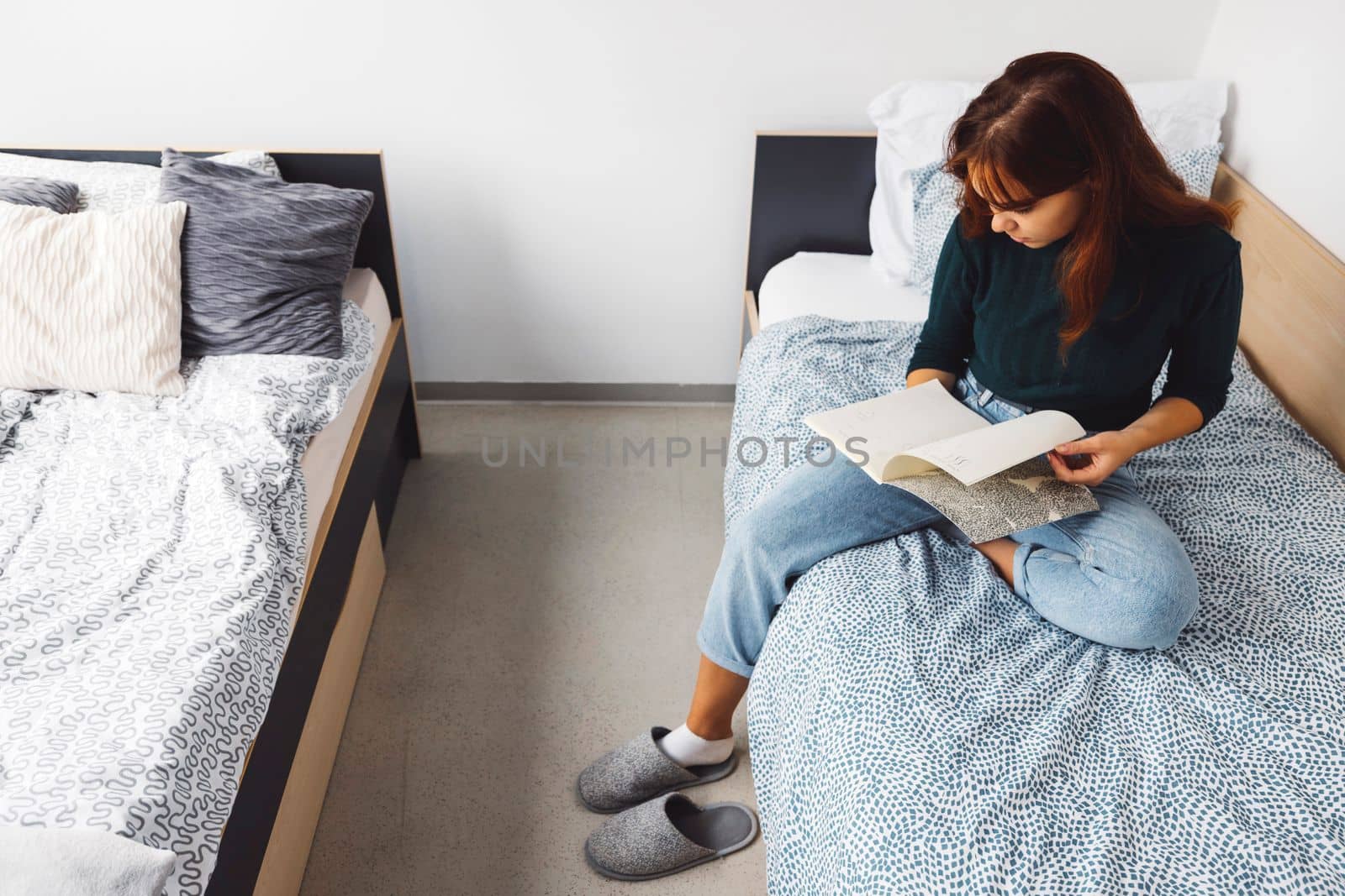 Young caucasian woman, college student studying in her dorm room, sitting on the bed. Bright room with lots of natural light. 