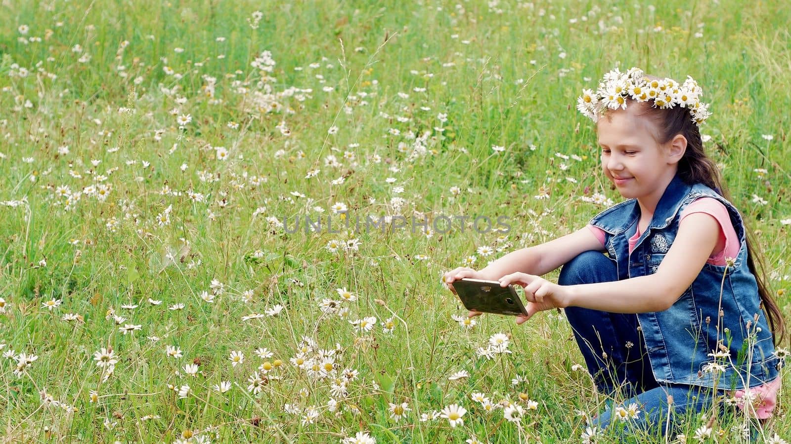 Little girl holding a phone, mobile, taking pictures of them, taking photos of a camomile lawn. High quality photo