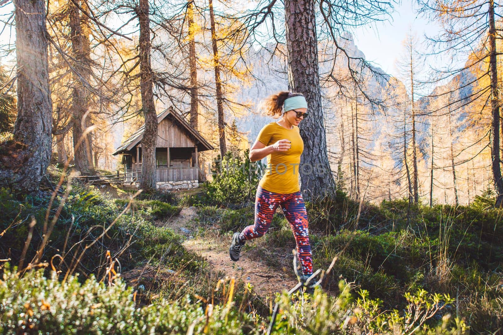 Joyful woman hiker running in the autumn forest, wearing an orange shirt and colorful leggings. Woman jumping in the air while hiking trough the forest. Sunny autumn hike.