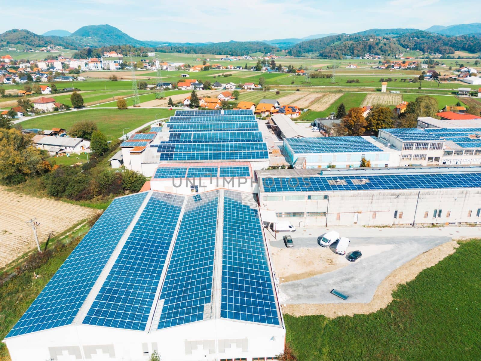 Solar panels installed on a roof of a large industrial building or a warehouse. Industrial building in the country side of Slovenia with residential houses in the background. High quality photo