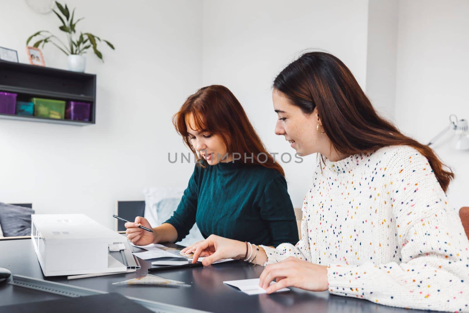 Two young caucasian women, college students studying together in their dorm room in a bright modern room. 