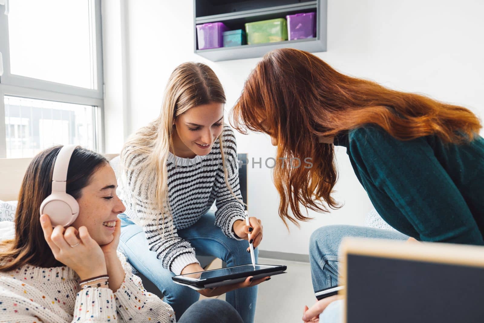 Group of three roommates, college student, young caucasian women, spending time together in their room, studying, talking, having fun, laughing. 