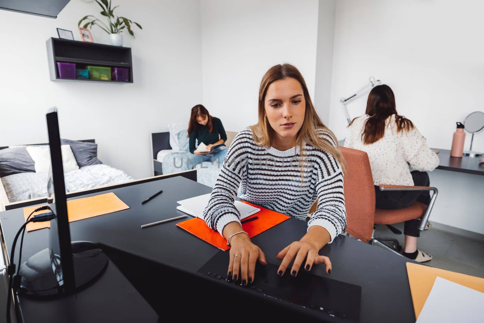 Young caucasian woman, college student studying in her dorm room, sitting by the desk. Bright room with lots of natural light. 