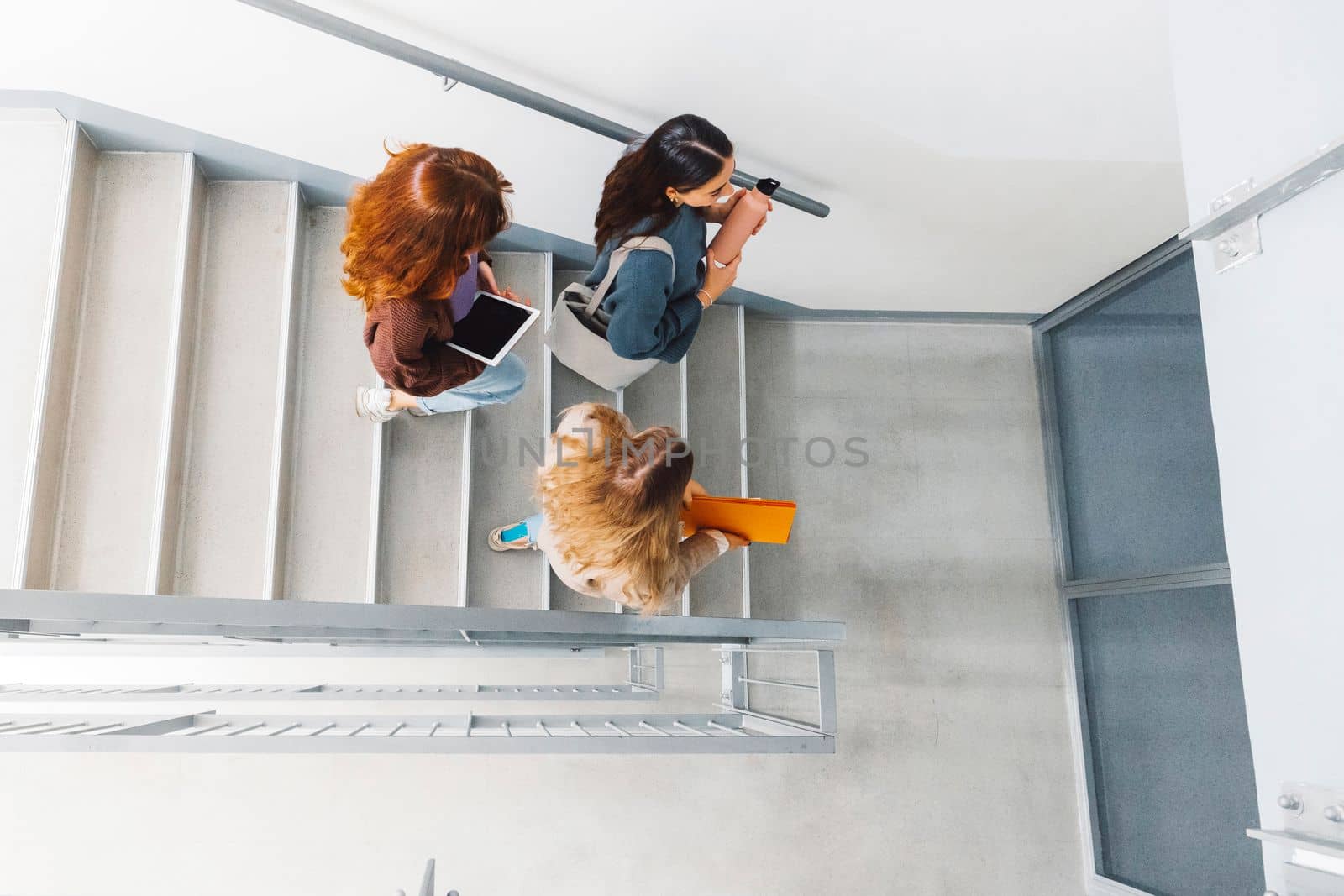 Top down view, three unrecognizable female students walking down the stairs to their classroom by VisualProductions