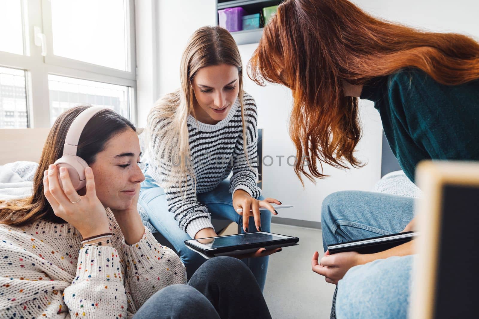 Group of three roommates, college student, young caucasian women, spending time together in their room, studying, talking, having fun, laughing. 