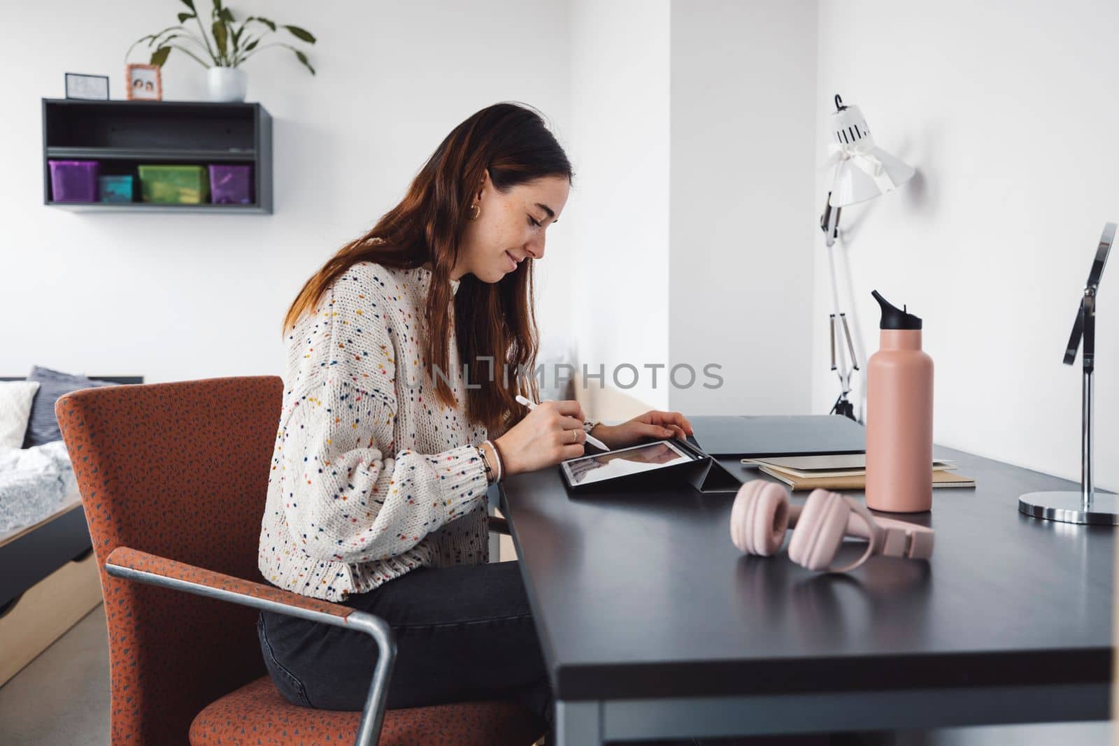 Young caucasian woman, college student studying in her dorm room, sitting by the desk. Bright room with lots of natural light. 