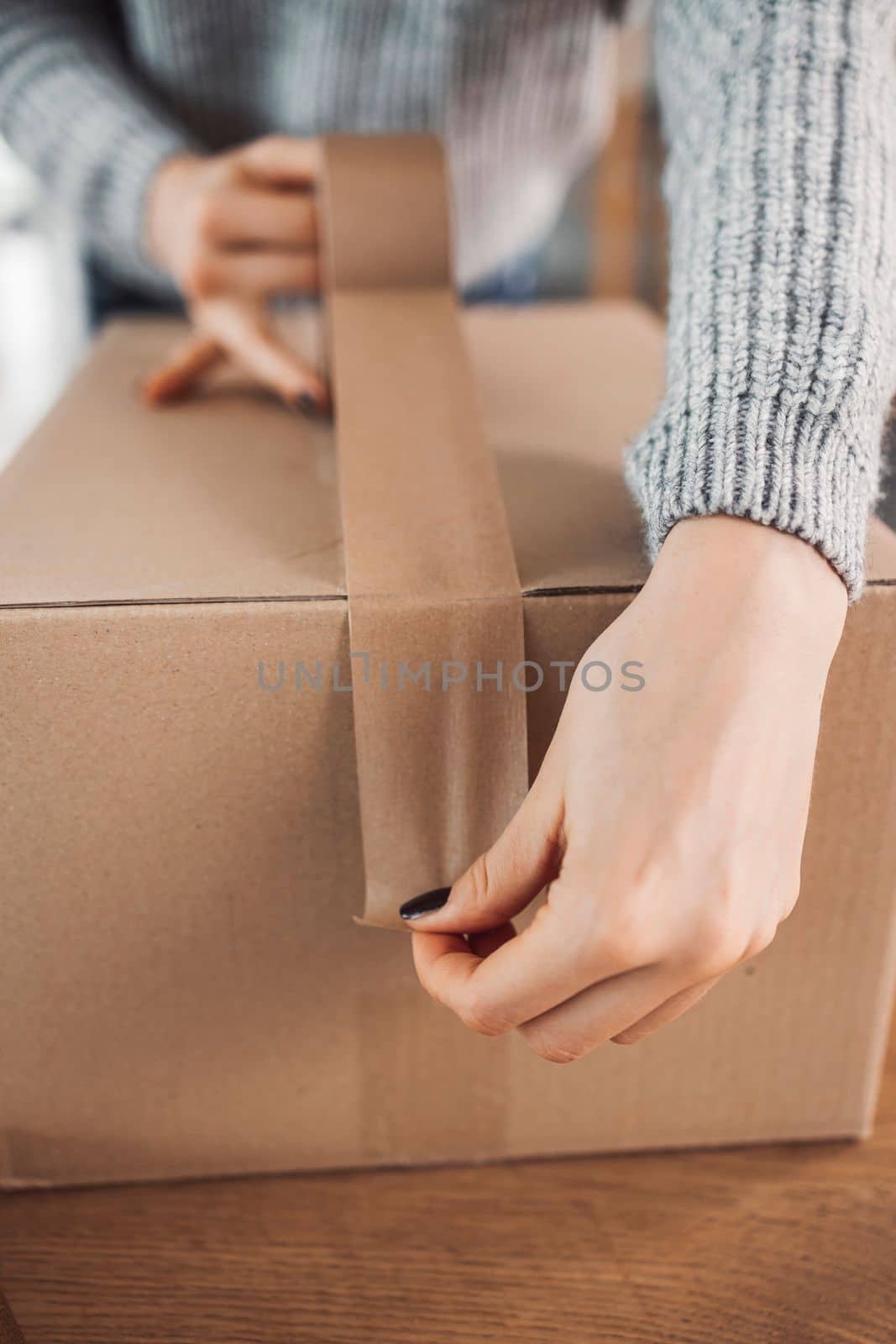 Young caucasian woman wrapping a gift, getting it ready to send in the post. Woman packaging a surprise gift for a family member, packaging it into a brown cardboard box.