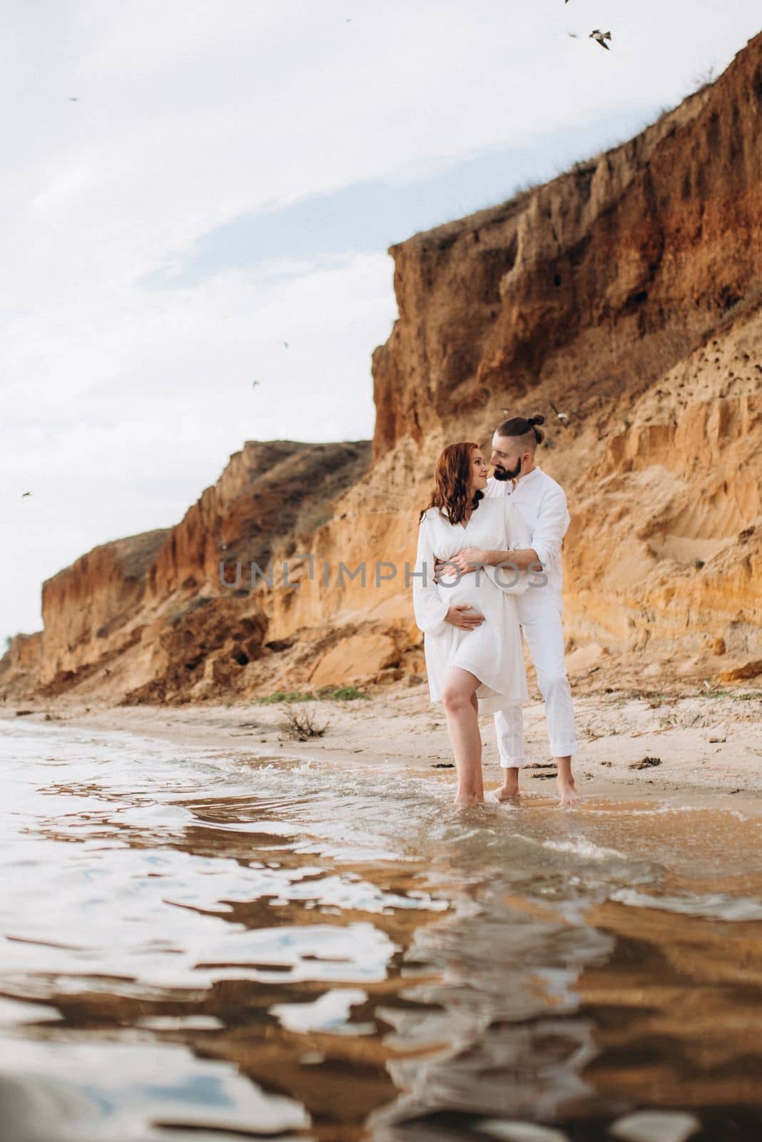 a guy with a girl in white clothes on the seashore next to clay cliffs