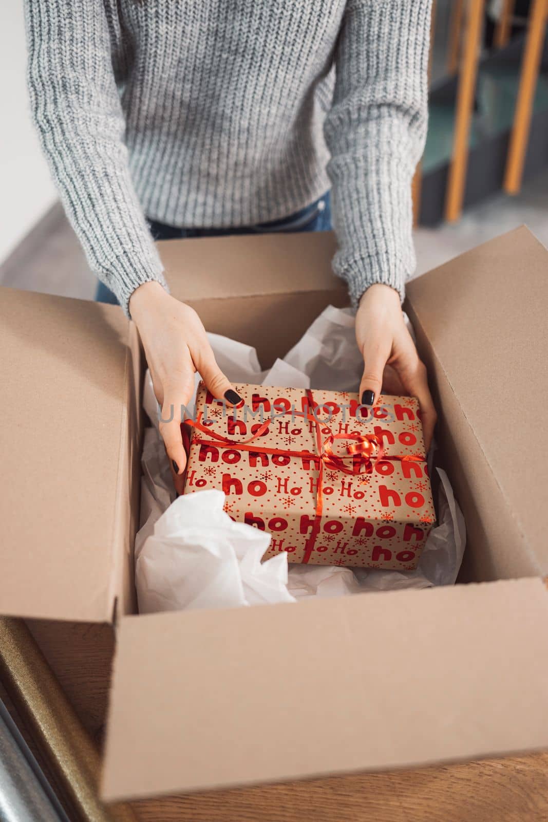 Young caucasian woman wrapping a gift, getting it ready to send in the post. Woman packaging a surprise gift for a family member, packaging it into a brown cardboard box.