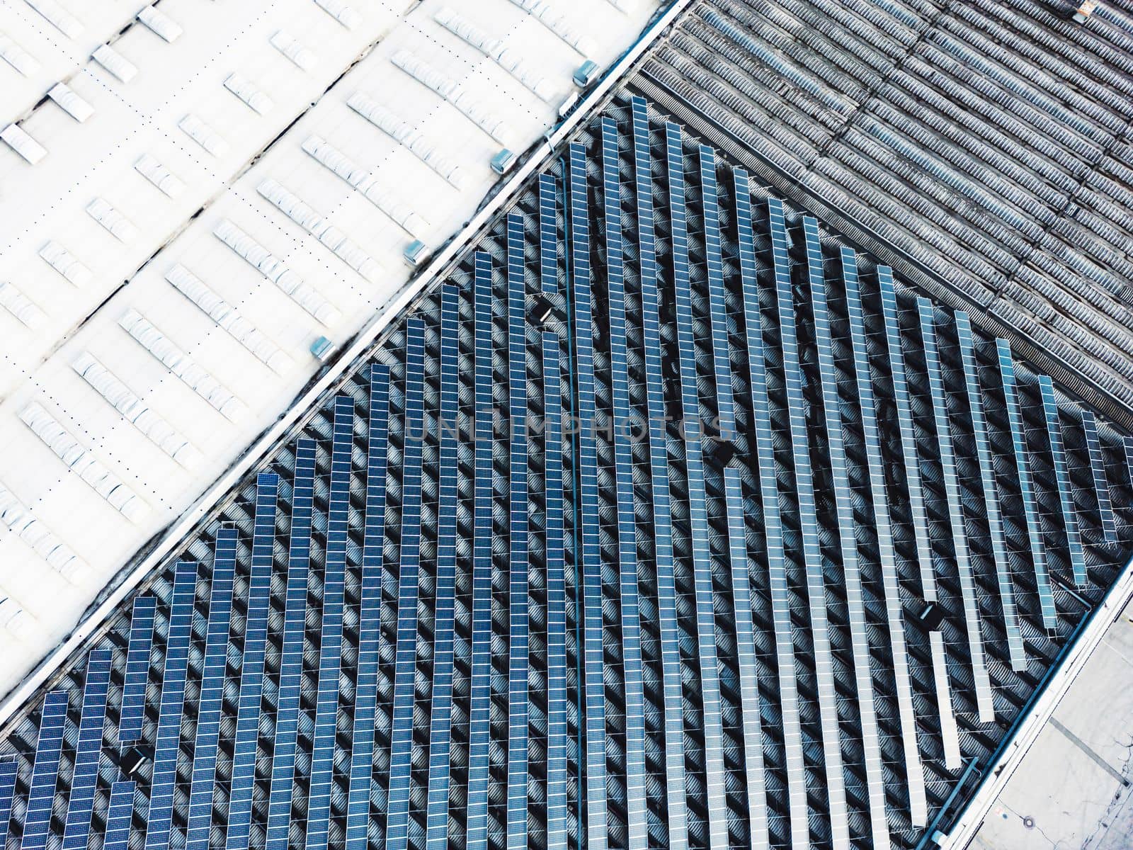 Aerial view of solar panels on industrial buildings. Drone point of view, flying over industrial area, with roof tops covered in solar panels.