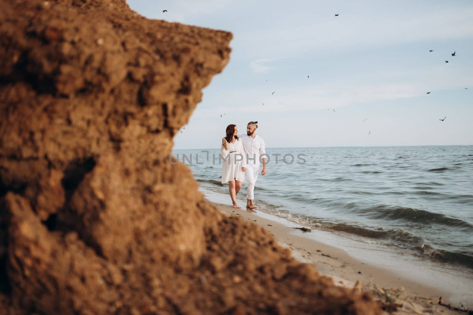 a guy with a girl in white clothes on the seashore next to clay cliffs