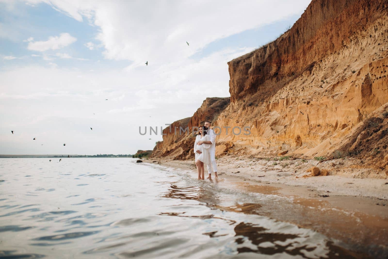 a guy with a girl in white clothes on the seashore next to clay cliffs