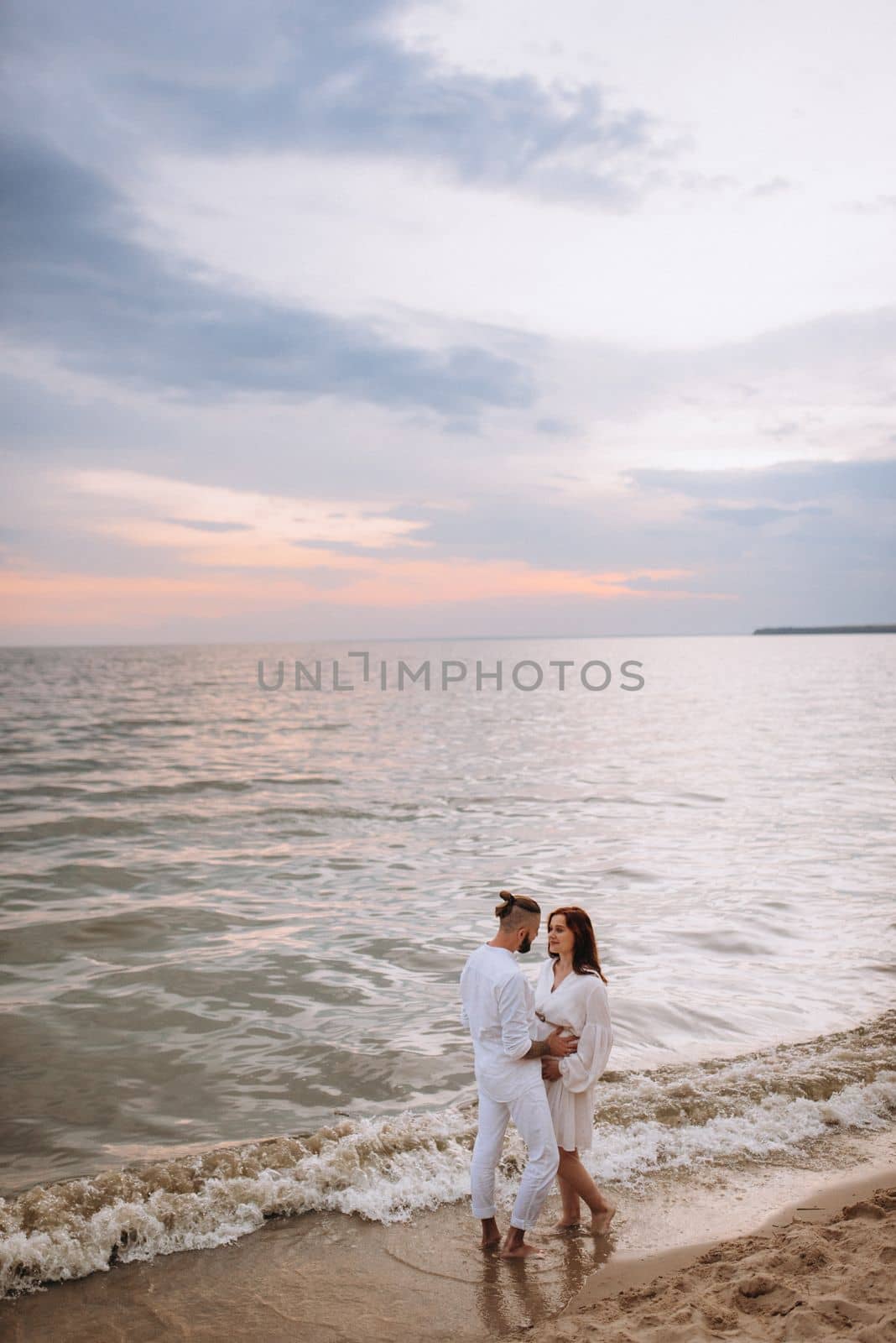 a guy with a girl in white clothes on the seashore next to clay cliffs