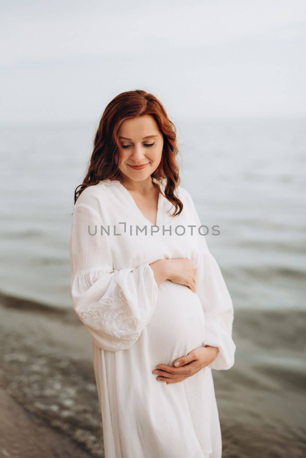 pregnant girl with brown hair on the seashore in white clothes