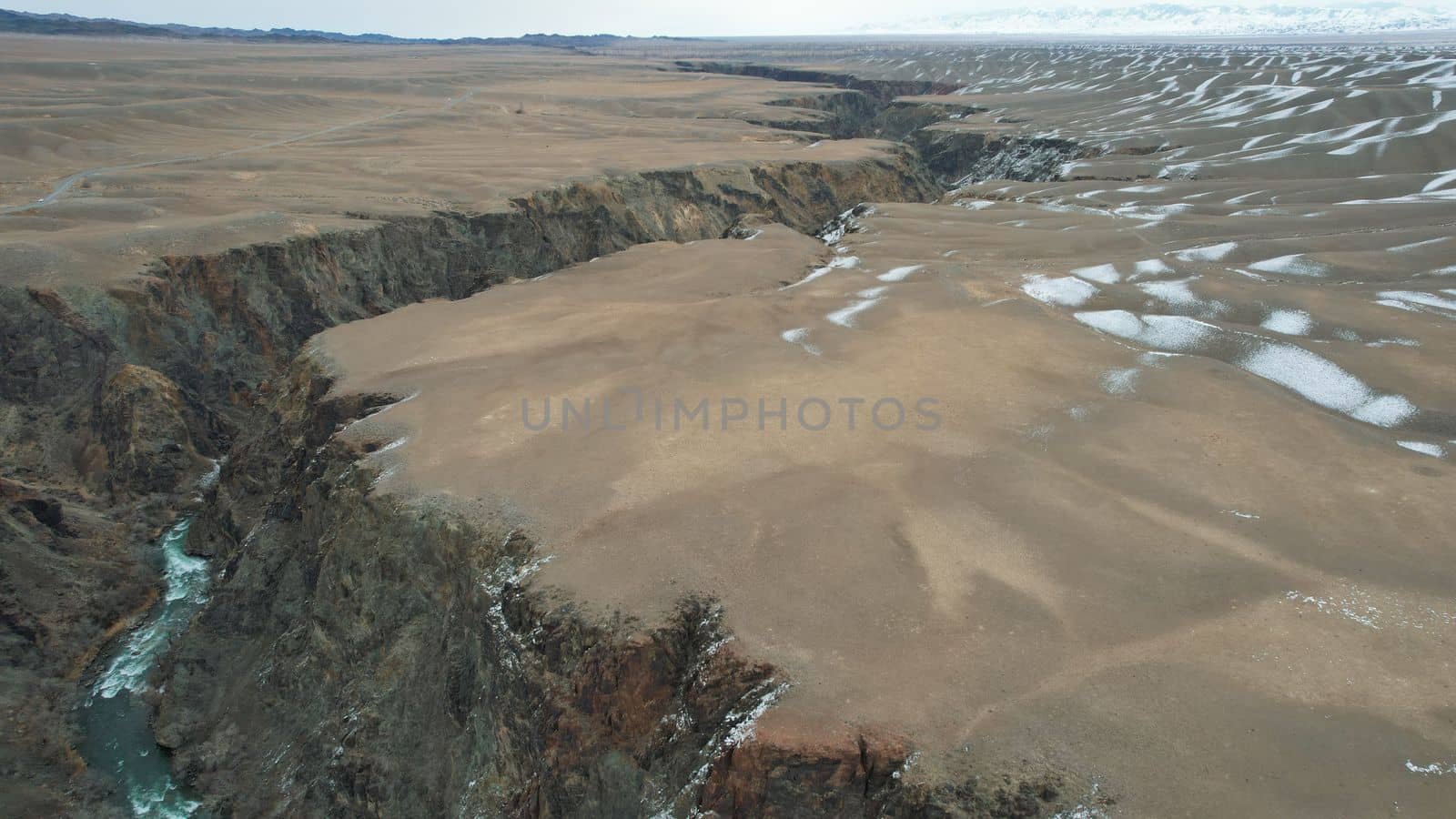 The Grand Canyon in the steppe with the emerald river. A crack in the ground with black stones, the green color of the river. Bushes grow in places. There are tourists and buses on edge. Kazakhstan