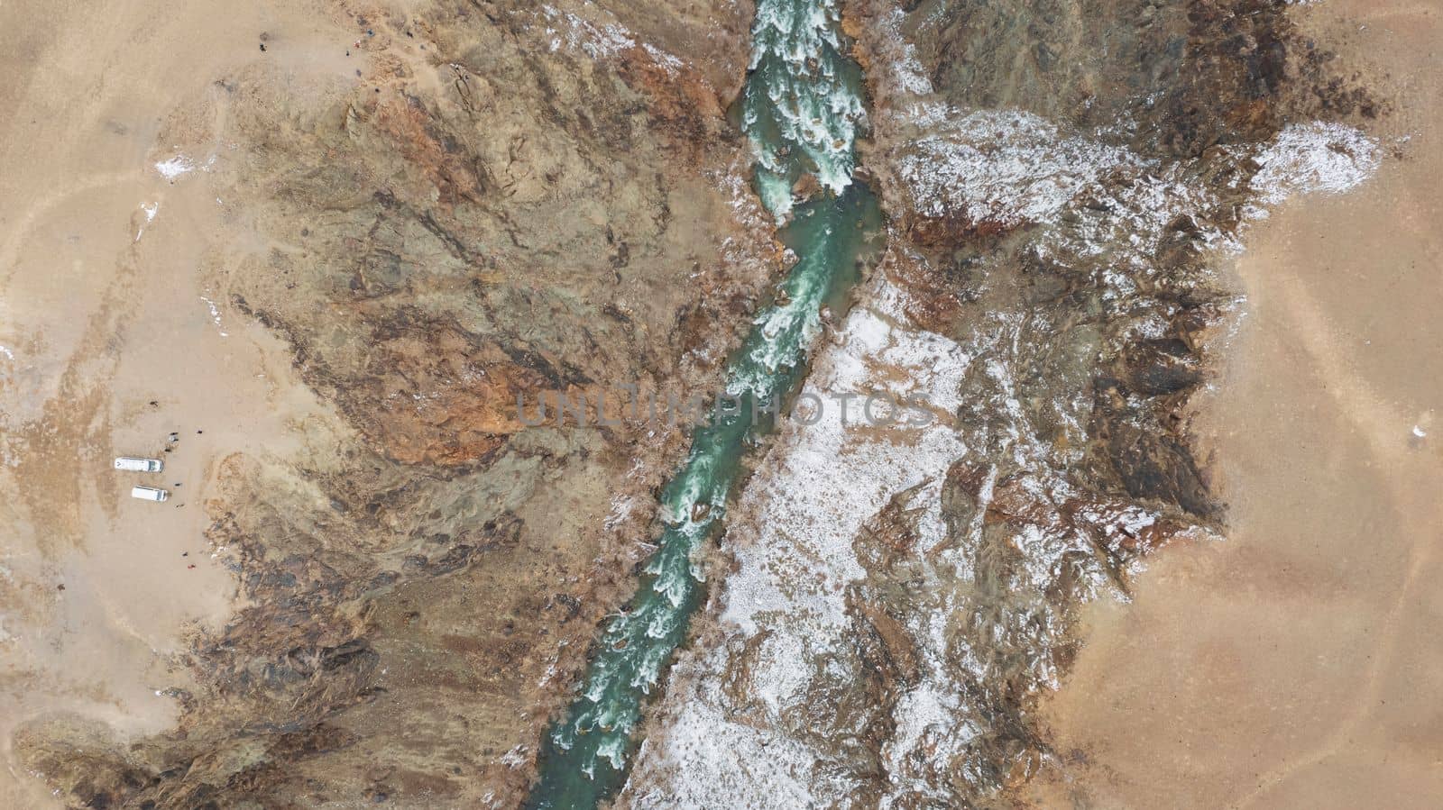 The Grand Canyon in the steppe with the emerald river. A crack in the ground with black stones, the green color of the river. Bushes grow in places. There are tourists and buses on edge. Kazakhstan