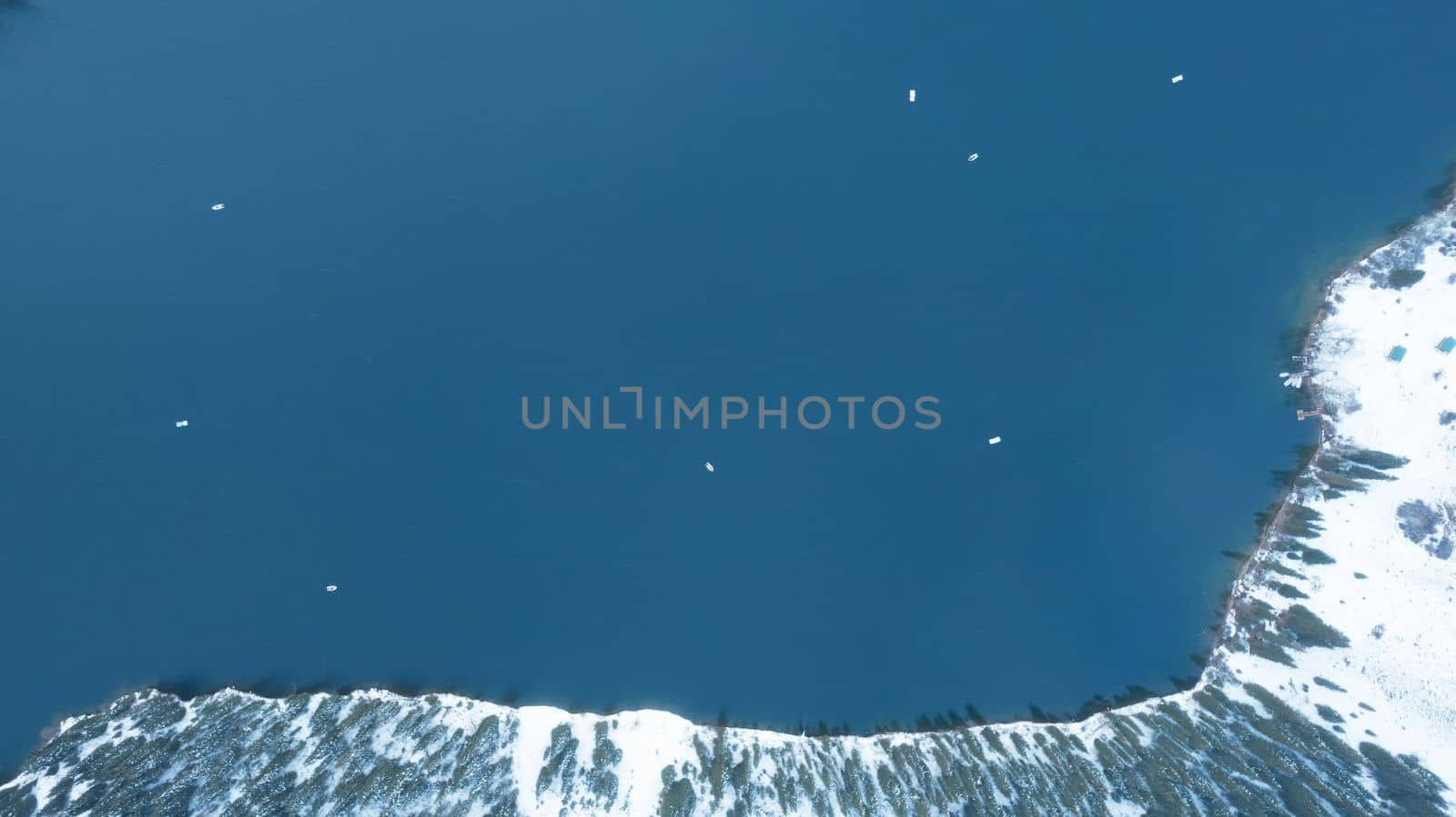 Kolsai mountain lake in the winter forest. Drone view of clouds, coniferous trees, mirrored smooth water, hills and mountains in the snow. Yellow sunset. Boats float in places. Top. Kazakhstan, Almaty