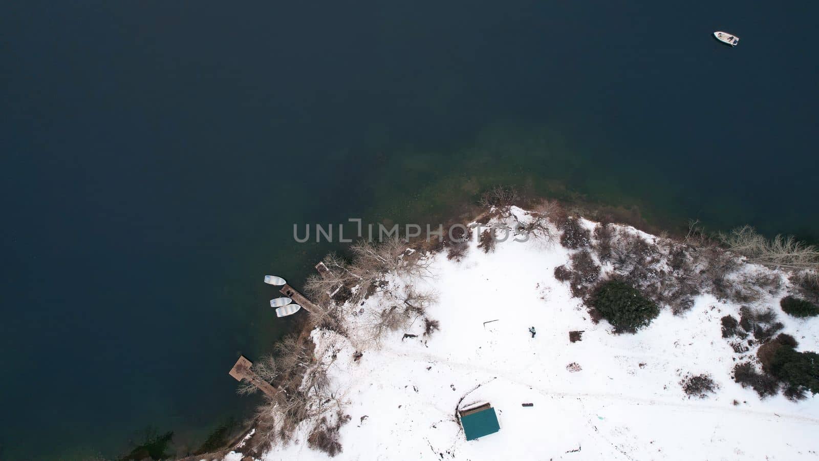 Kolsai mountain lake in the winter forest. Drone view of the pier with boats, trees, clear smooth water, snow lying on the ground. People swim in white boats. Kazakhstan, Almaty