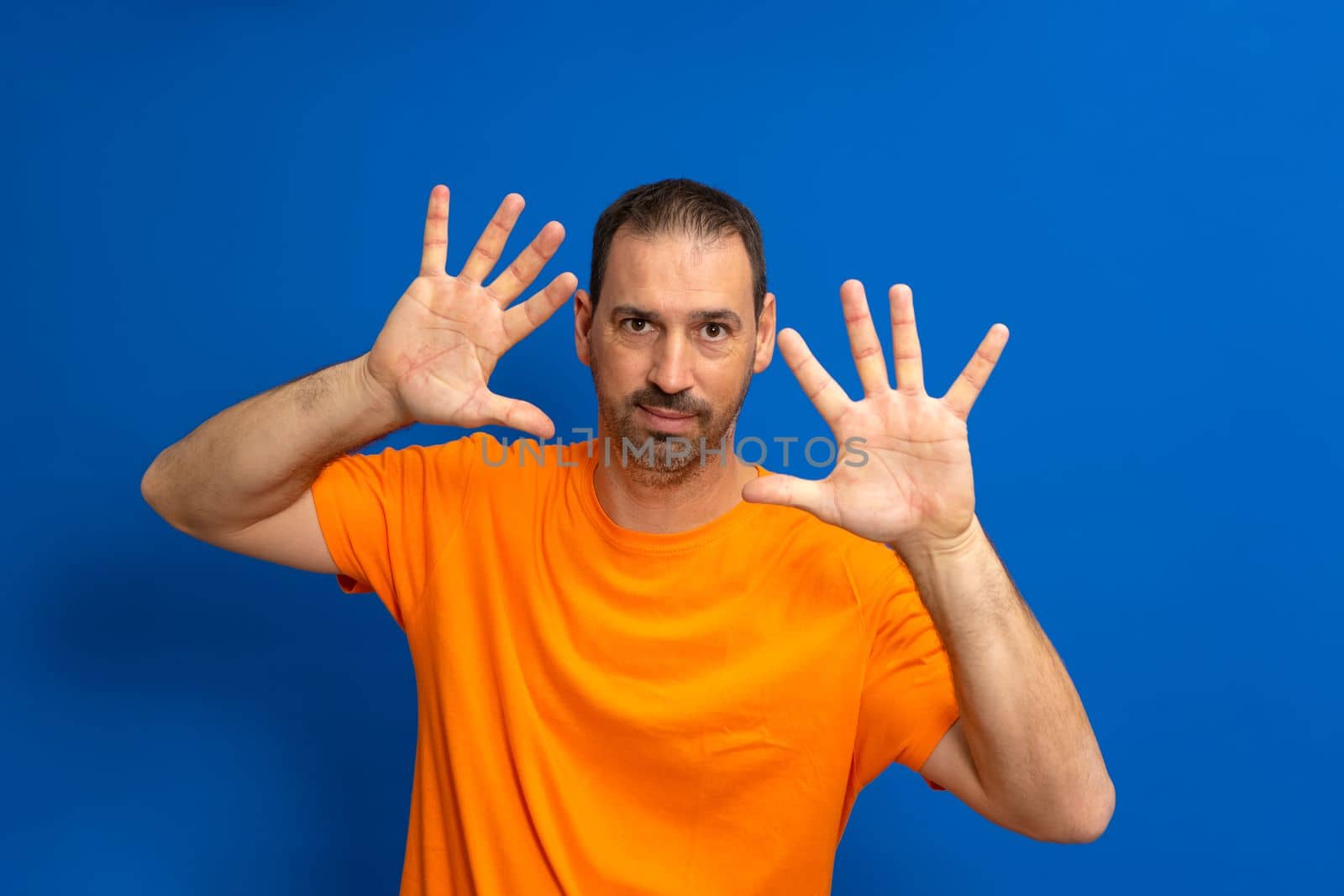 Front view of a Caucasian man with short hair wearing an orange t-shirt with his palms facing him, camera facing palm, touching an interactive virtual screen