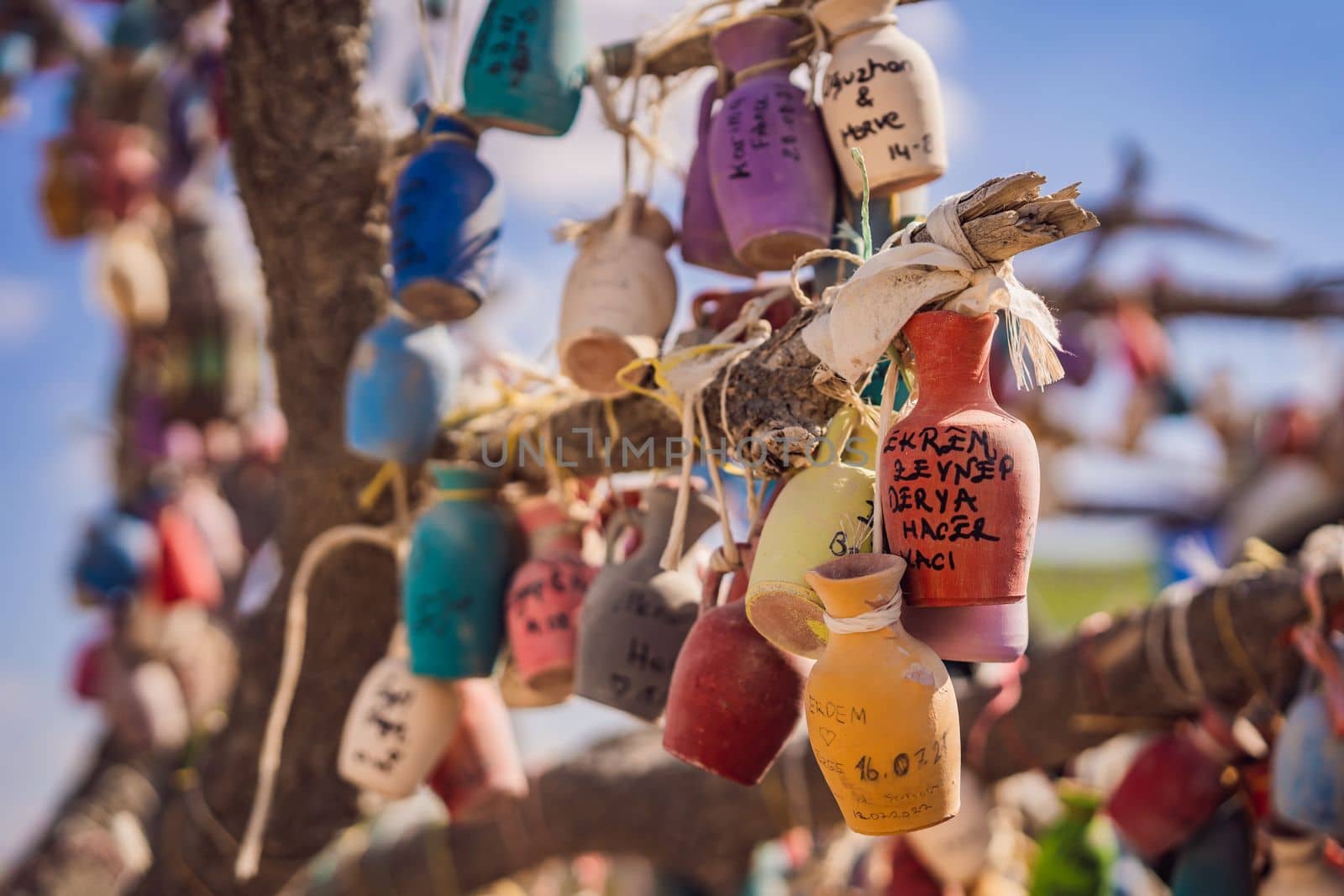 Wish tree. Small multi-colored jugs with inscriptions, wishes hanging on the branches of a tree., against the backdrop of sand ruins and blue sky.